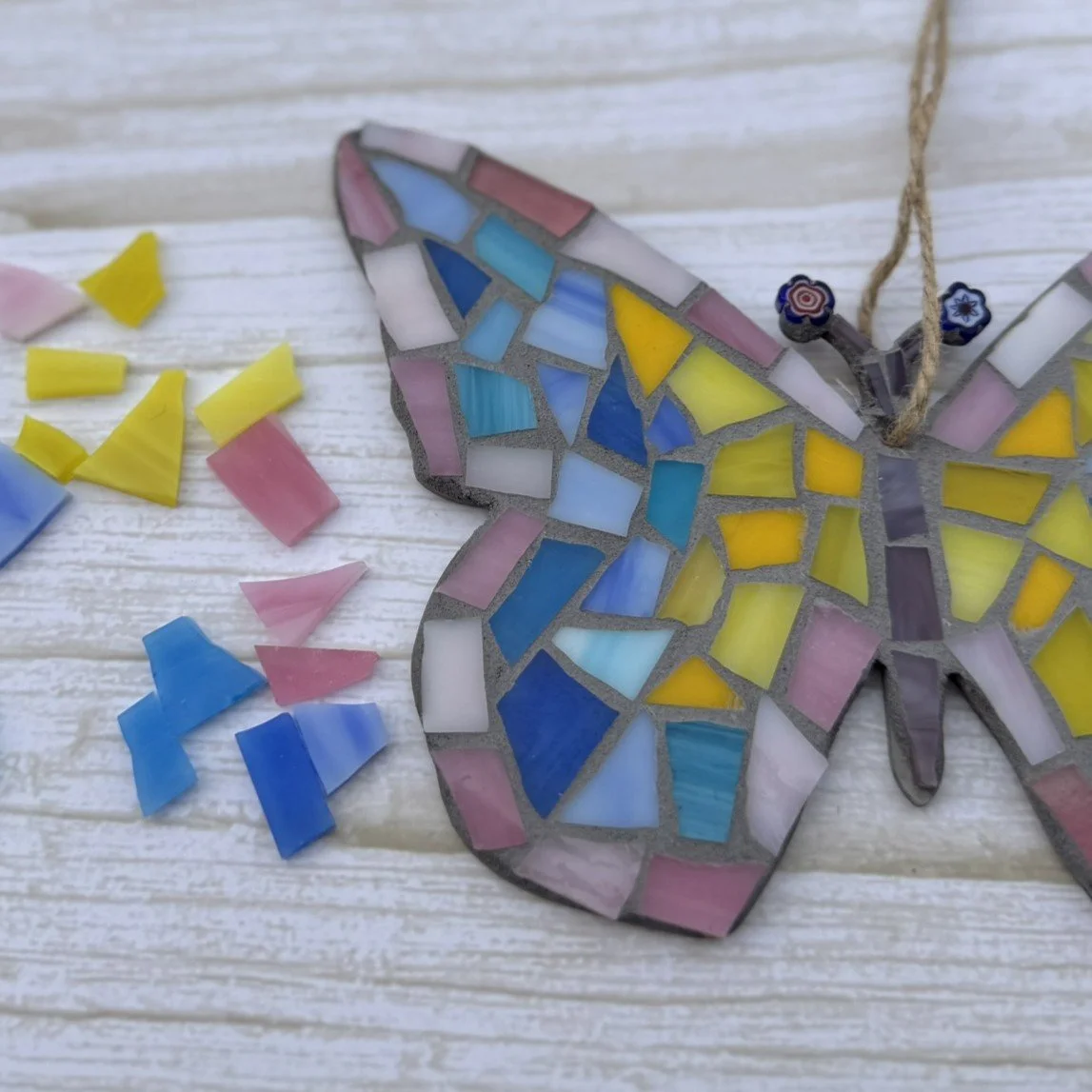 Colorful mosaic butterfly ornament with scattered mosaic pieces on a white wooden surface.