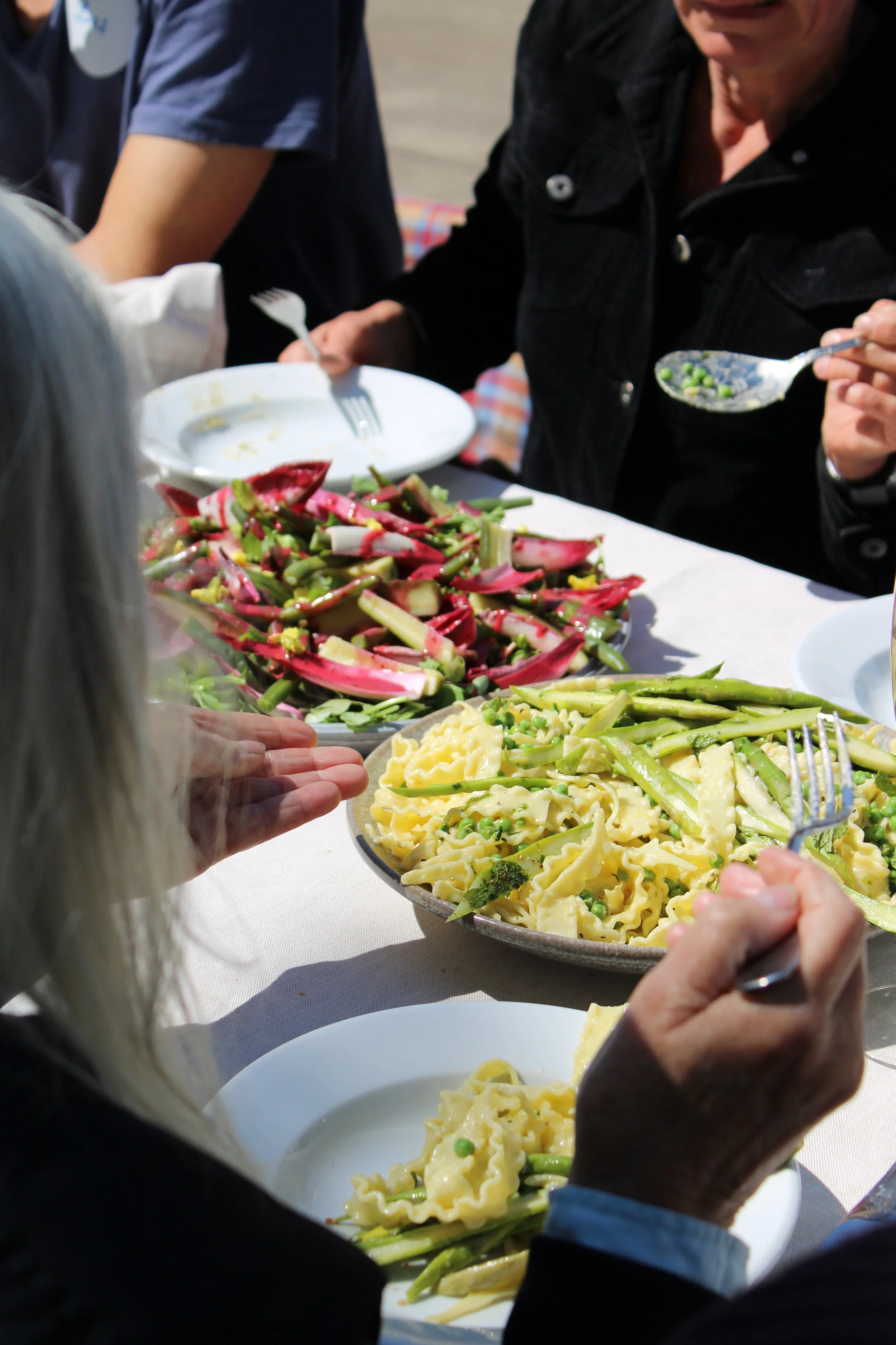 Mensen die genieten van een maaltijd met pasta en salades, dineren buiten onder de zon.