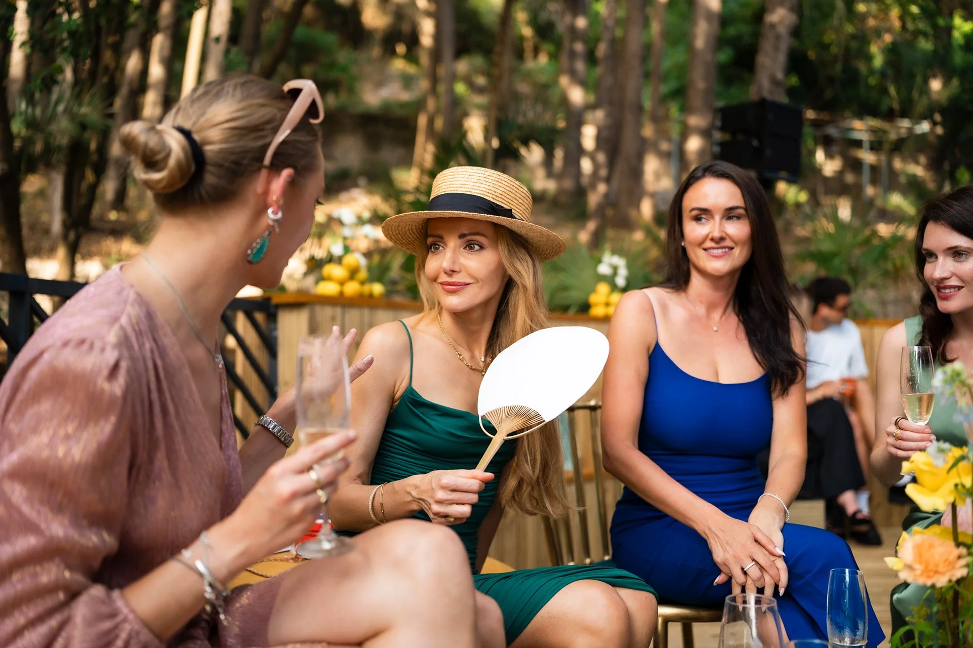 Group of women chatting at an outdoor celebration, with flowers and drinks on the table.