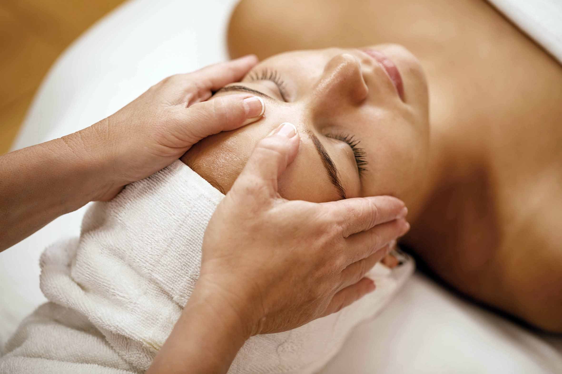 A person receiving a facial massage from a massage therapist in a spa setting.