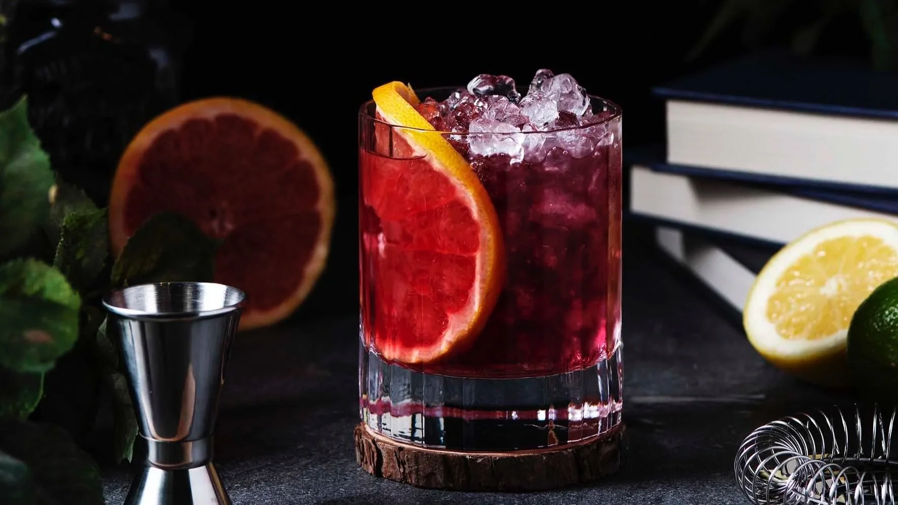 a rimmed glass full with ice and negroni and a slice of orange. a spirit measure in the foreground
