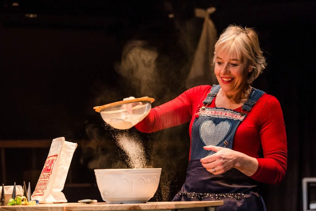 Danyah Miller in red jumper and denim apron shaking flour in a sieve