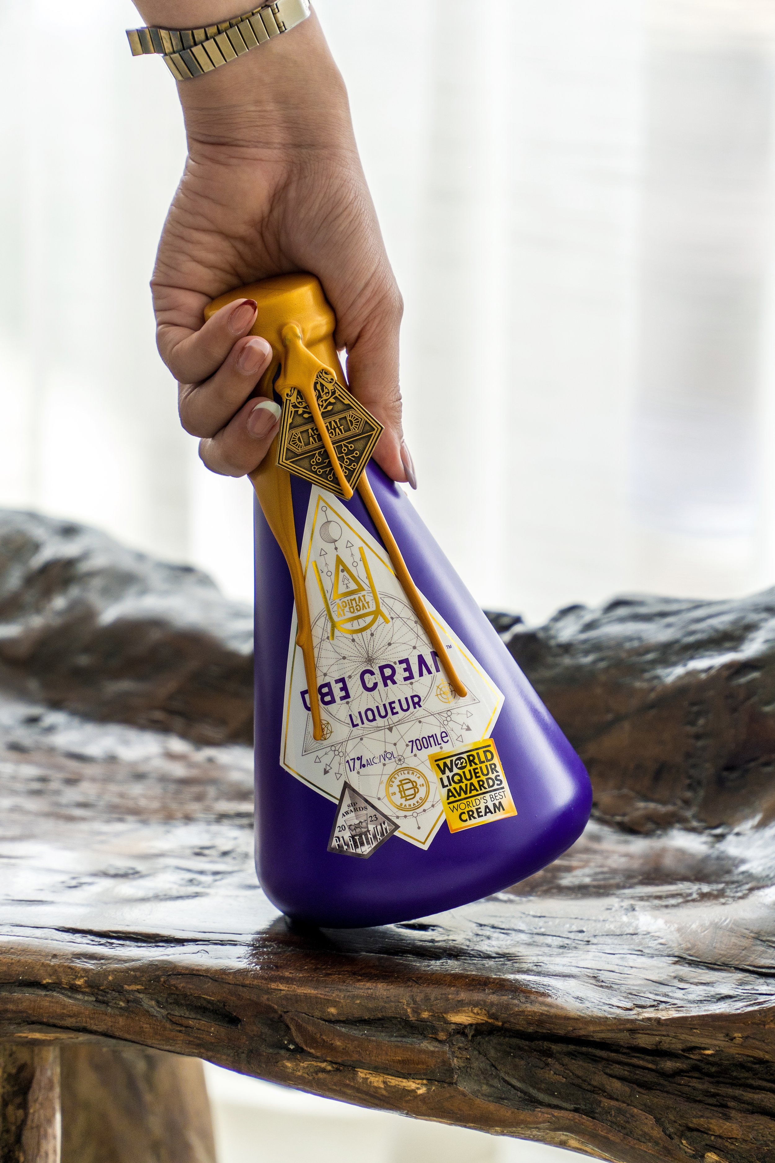 Hand holding a purple bottle of creamed liqueur on a wooden surface.