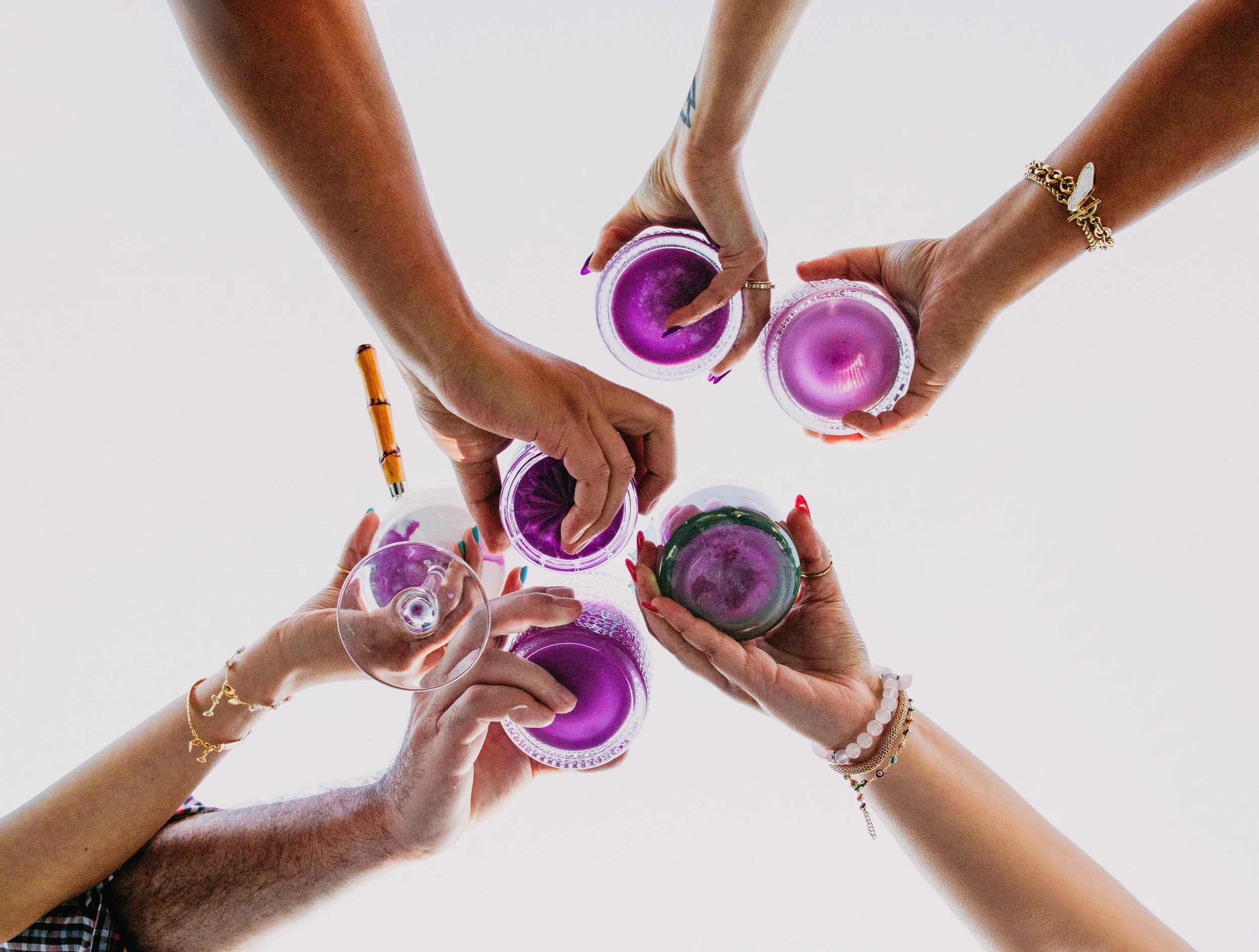 Six people holding glasses of purple drinks, seen from below against a white background.
