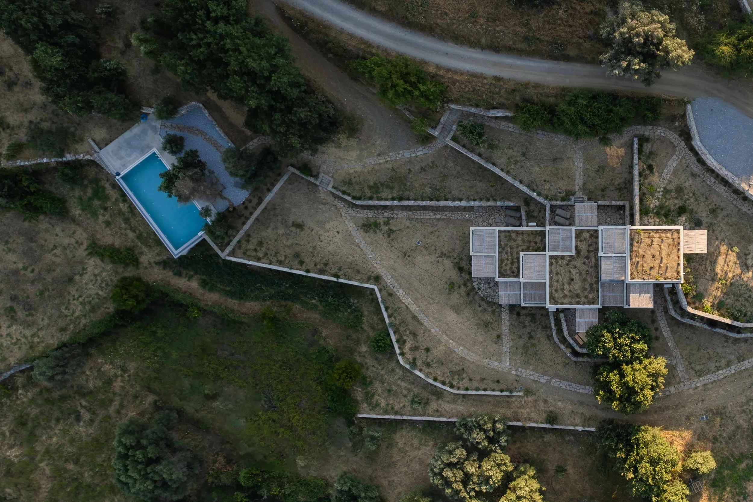 Modern house with stone and concrete exterior, surrounded by greenery, with mountains in the background.