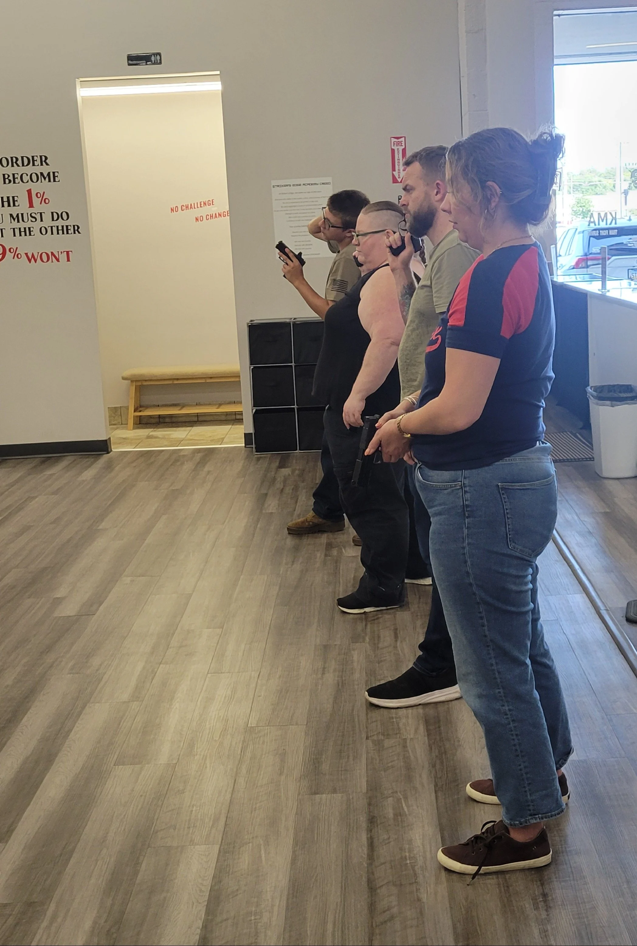 Five people standing in a line inside a store, holding firearms, practicing trigger control.
