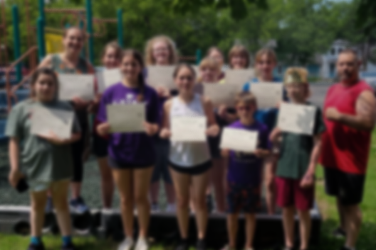 Group of children and adults holding certificates outdoors near playground equipment during daytime