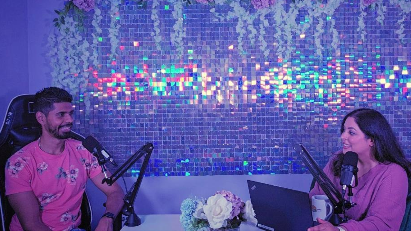 Couple sitting at desk with two mics hosting a podcast.