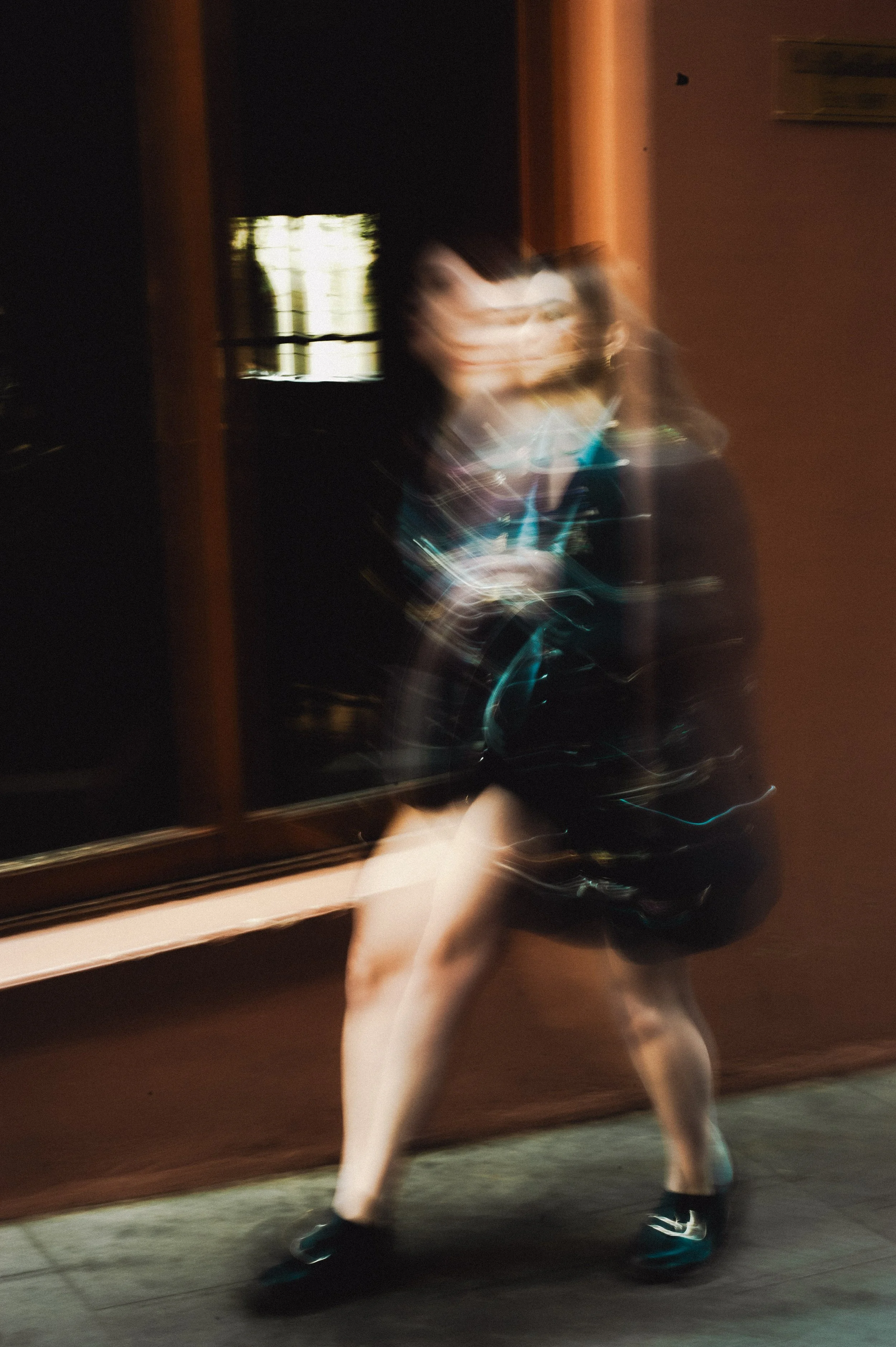 Blurred image of a person standing outside at night, wearing a dark zip-up hoodie, shorts, and sneakers, with streaks of light indicating motion.