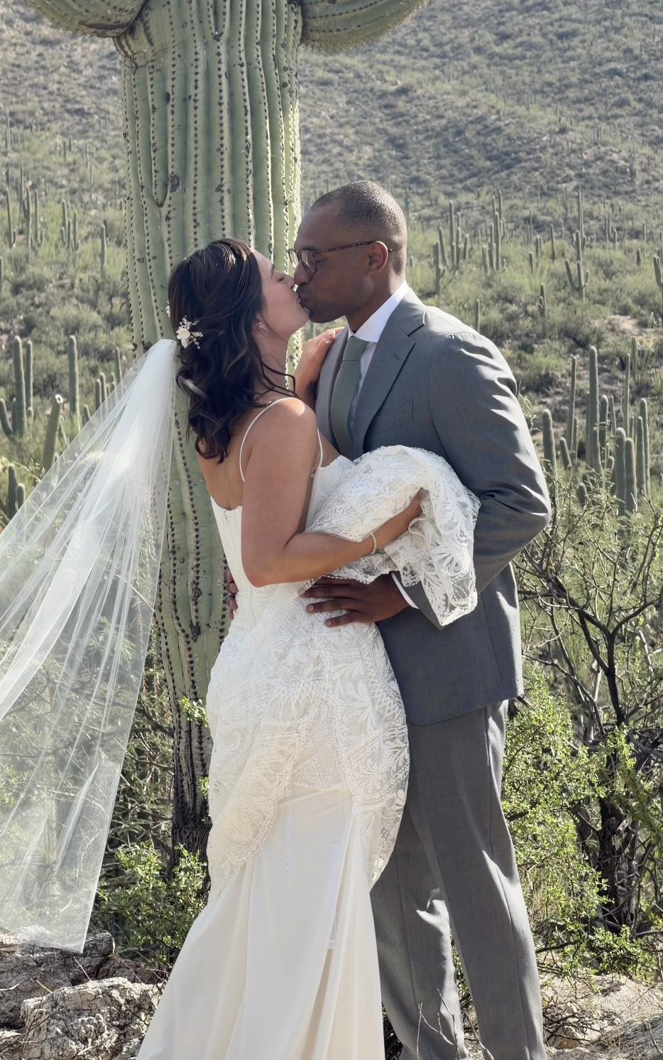 A bride and groom kiss in a desert landscape with cacti.