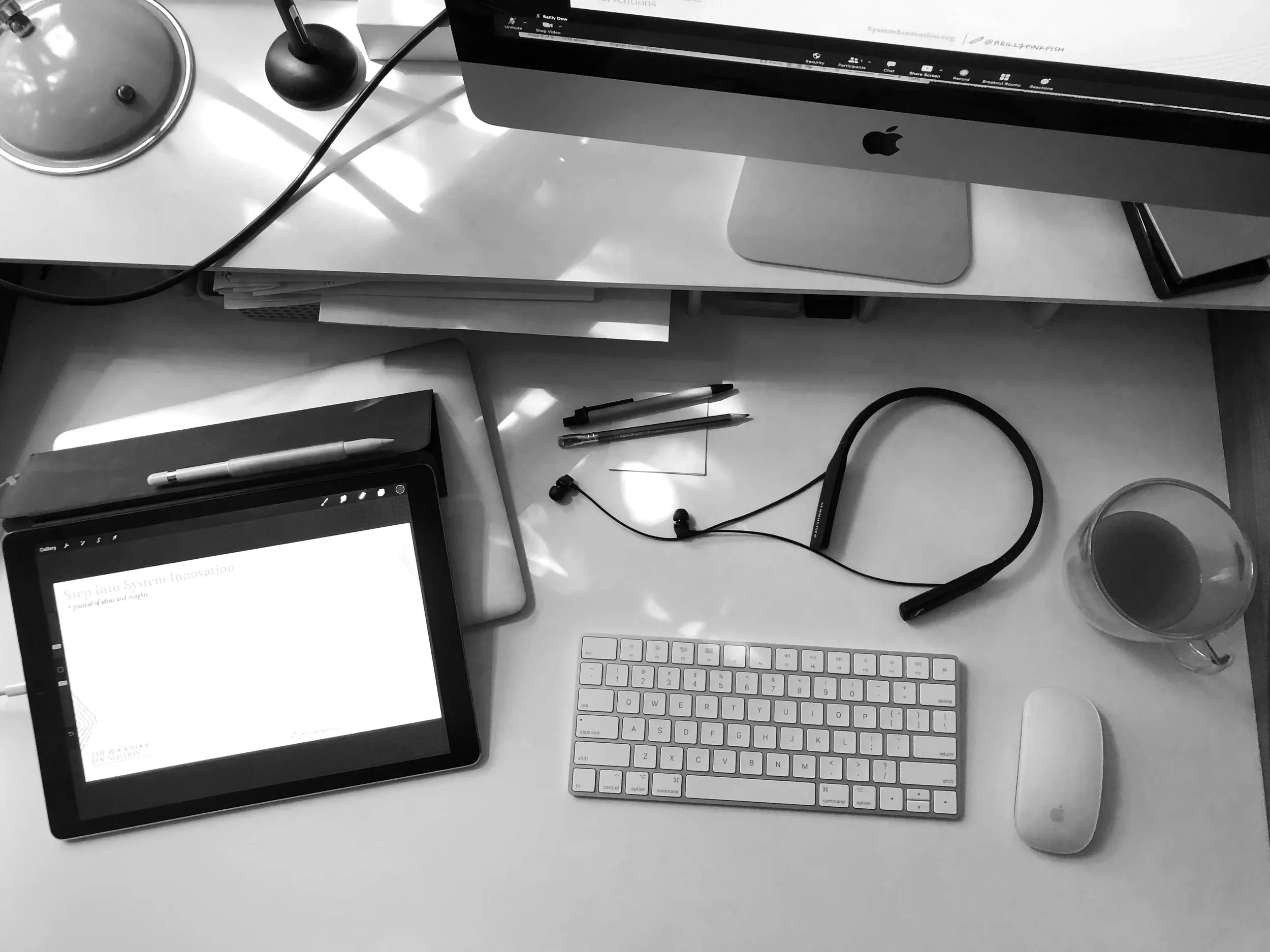 A keyboard, computer, iPad, and headphones on Reilly's desk, along with pens and a cup of coffee.