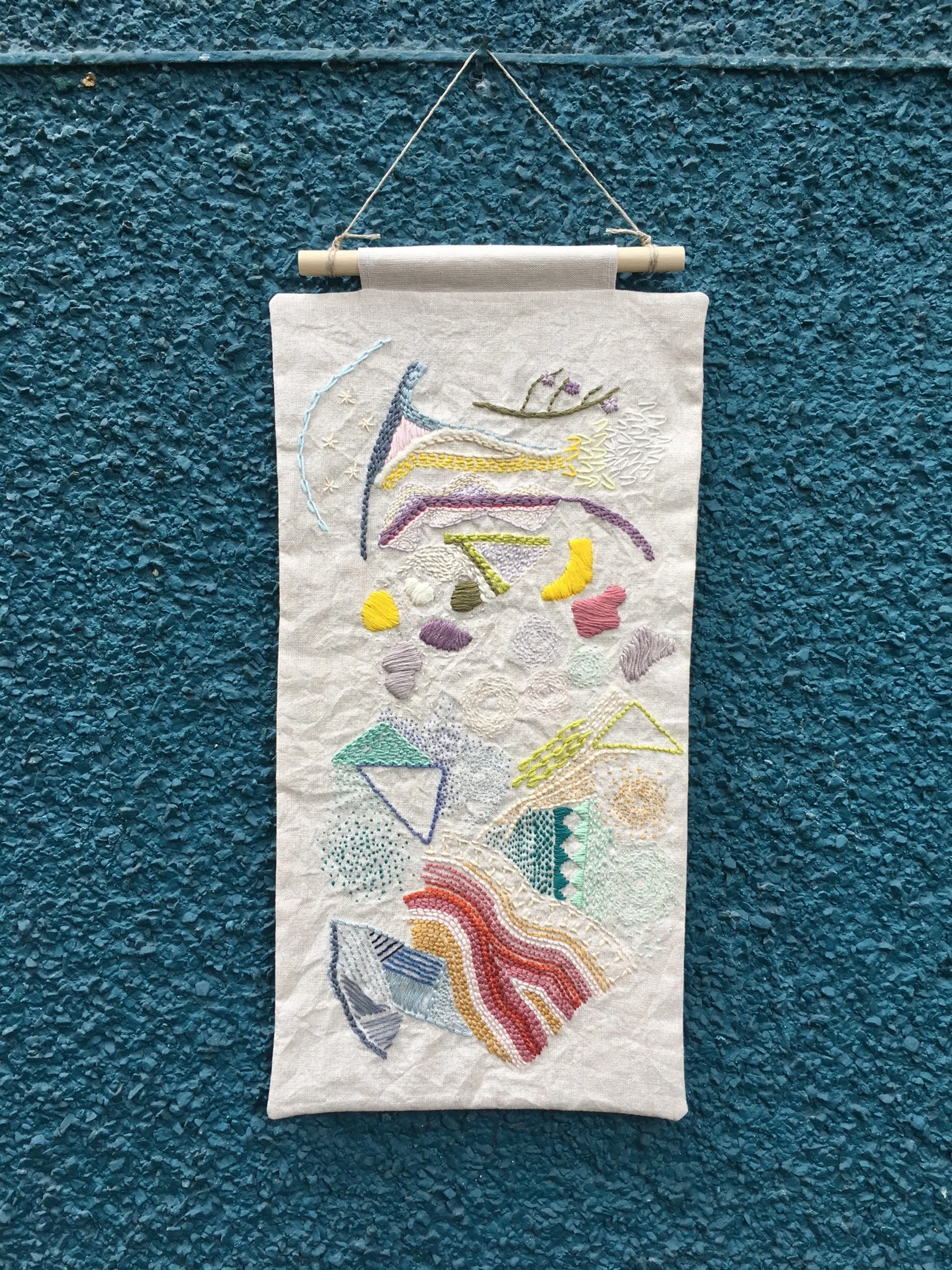Embroidered rectangular wall hanging on a textured blue background.