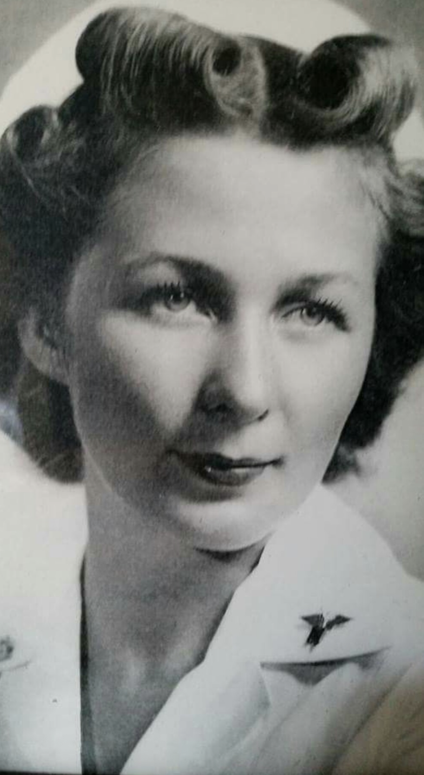 Black and white portrait photograph of a young woman with curled hair, wearing a light-colored jacket with a star-shaped pin on the lapel, looking slightly to her right.