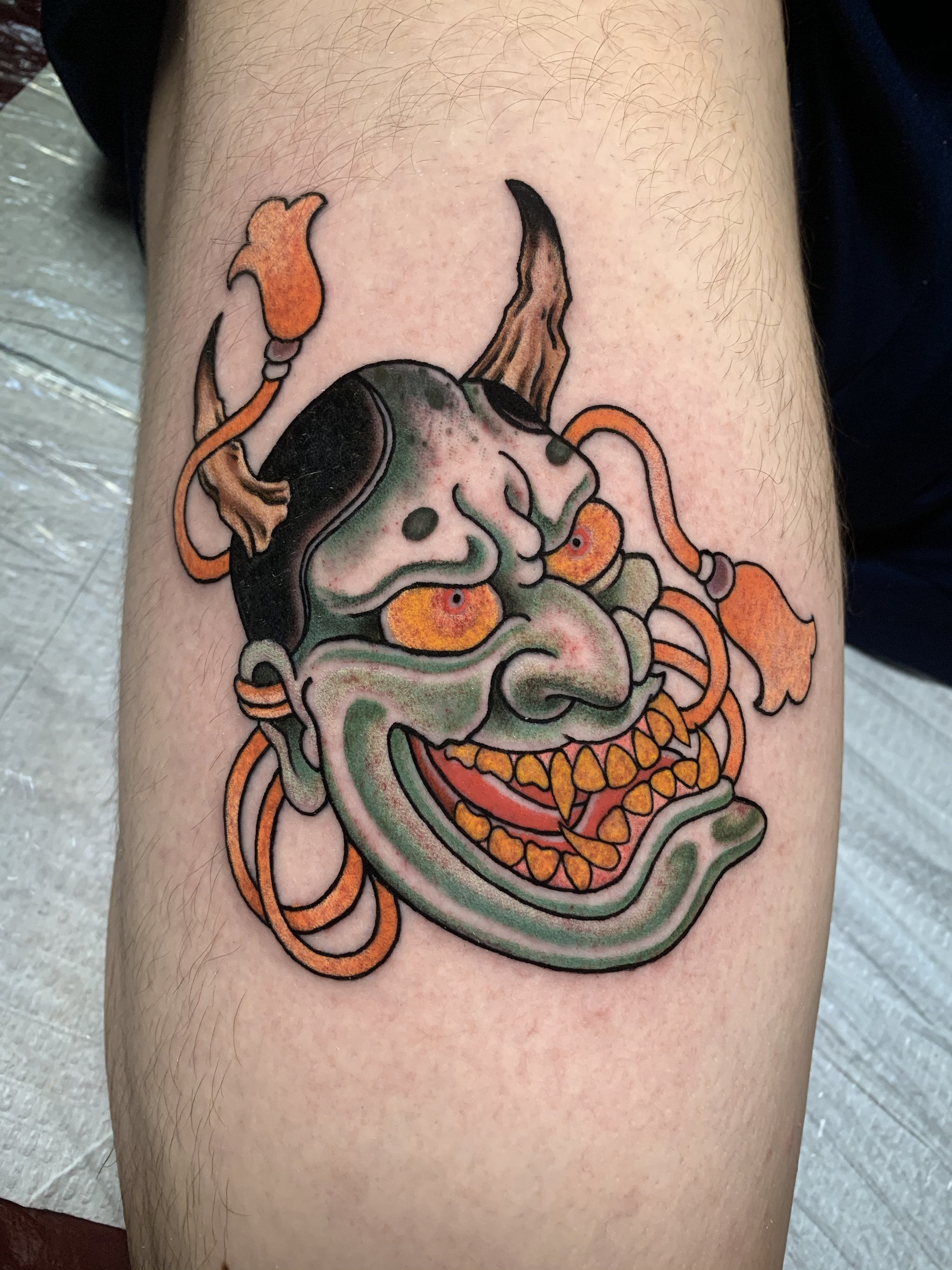 "Neo-traditional Hannya mask tattoo by Jon Santos, featuring bold outlines, vibrant colors, and intricate ornamental details. This design blends traditional Japanese symbolism with a modern twist, showcasing expert shading and dynamic composition. Pe