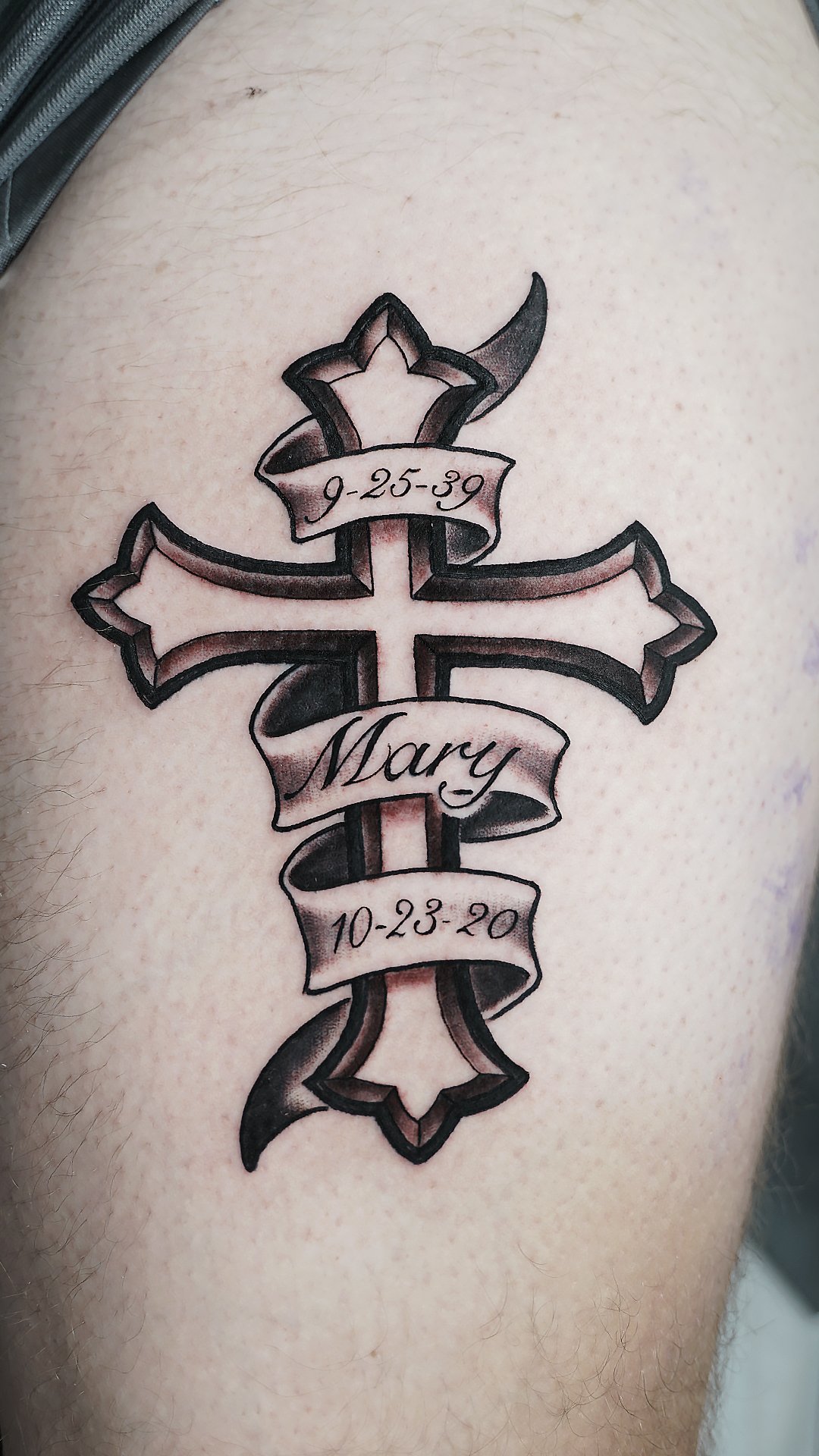 Custom cross tattoo with a name inscription by Jon Santos, blending bold lines and subtle shading for a timeless design. This personalized piece highlights expert craftsmanship and meaningful detail, perfect for clients seeking elegant, custom tattoo