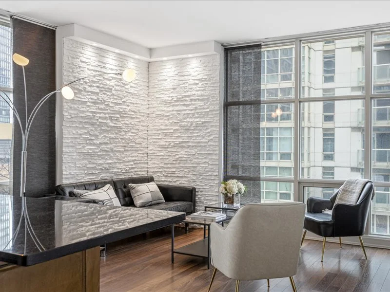 Front view of a two-story house with a small front yard, a sidewalk leading to the door, shrubs, and a wooden fence on the right side, with trees in the background.