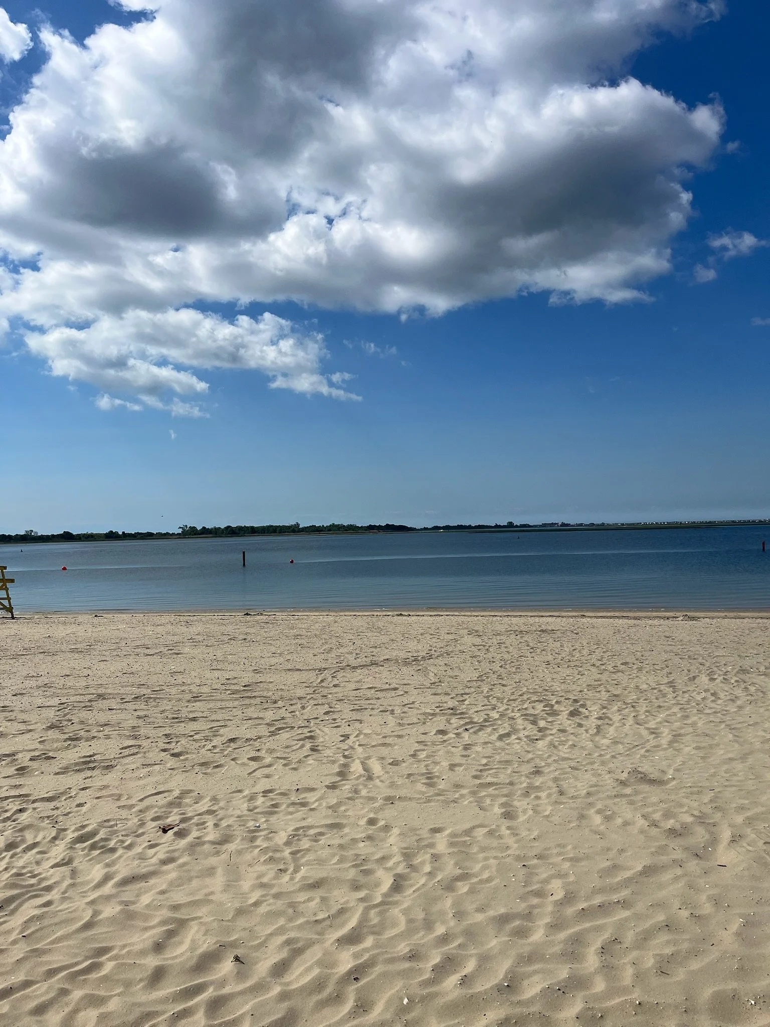 Landscape image of tan sand under deep blue sky with fluffy white and gray clouds