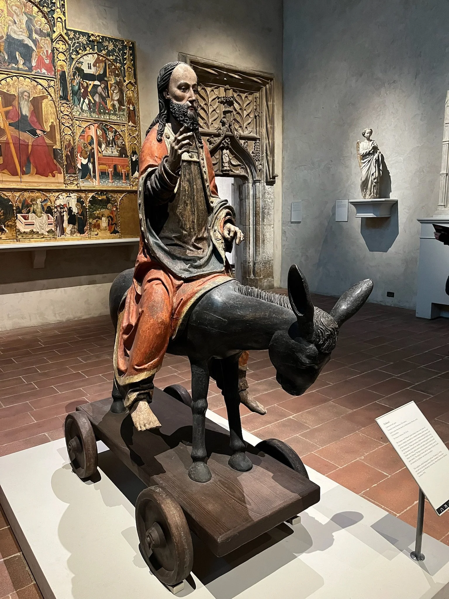 Statue of Jesus riding a donkey in front of medieval artwork