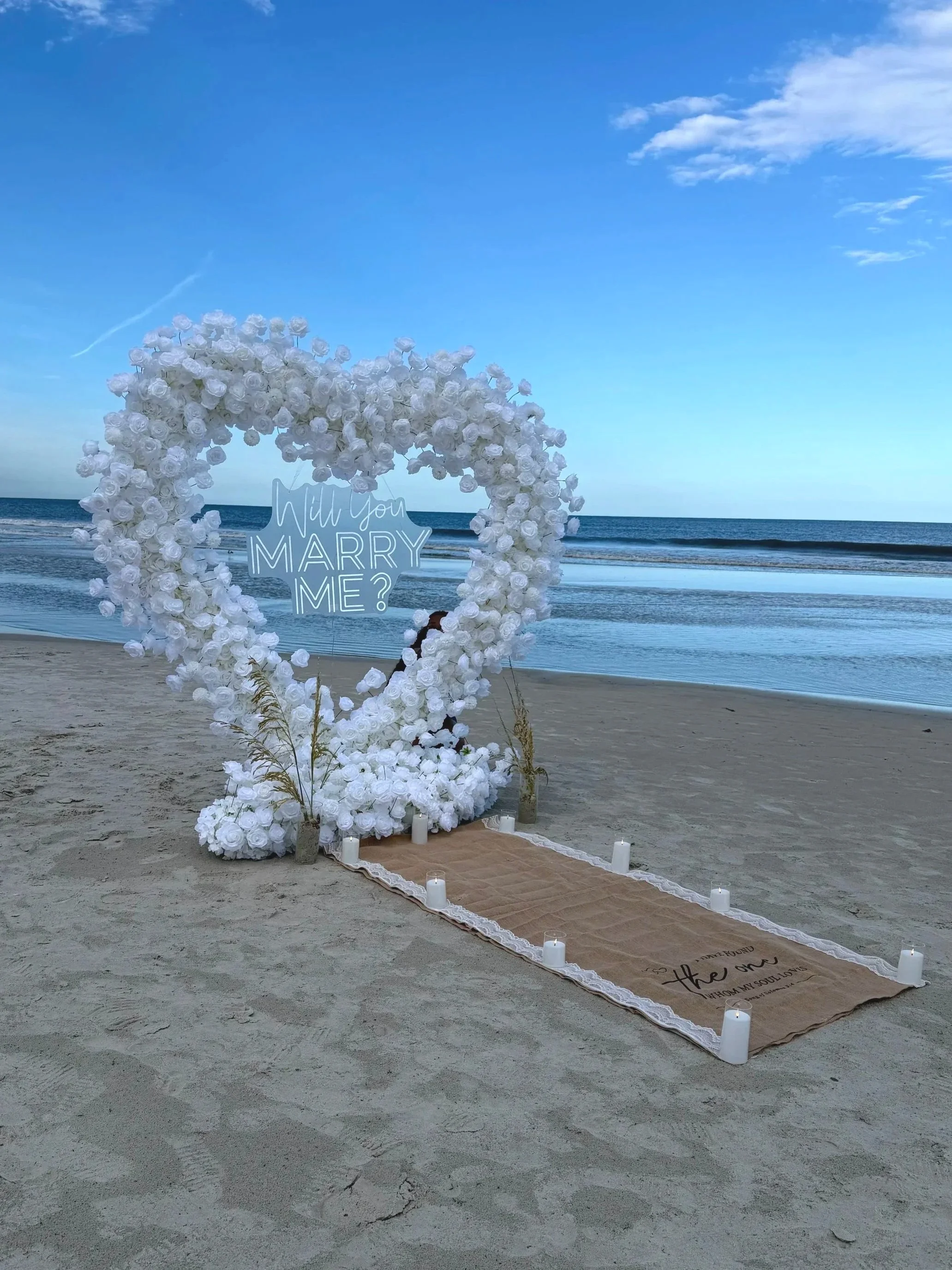 Proposal flower arch and LED sign that says "Will You Marry Me?" at the beach