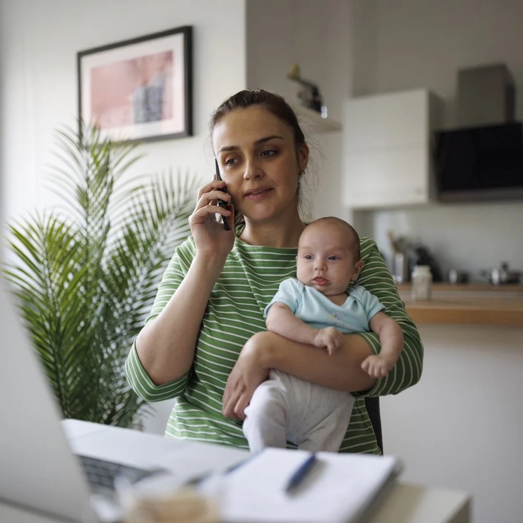 Woman holding a baby while talking on the phone in a modern kitchen.
