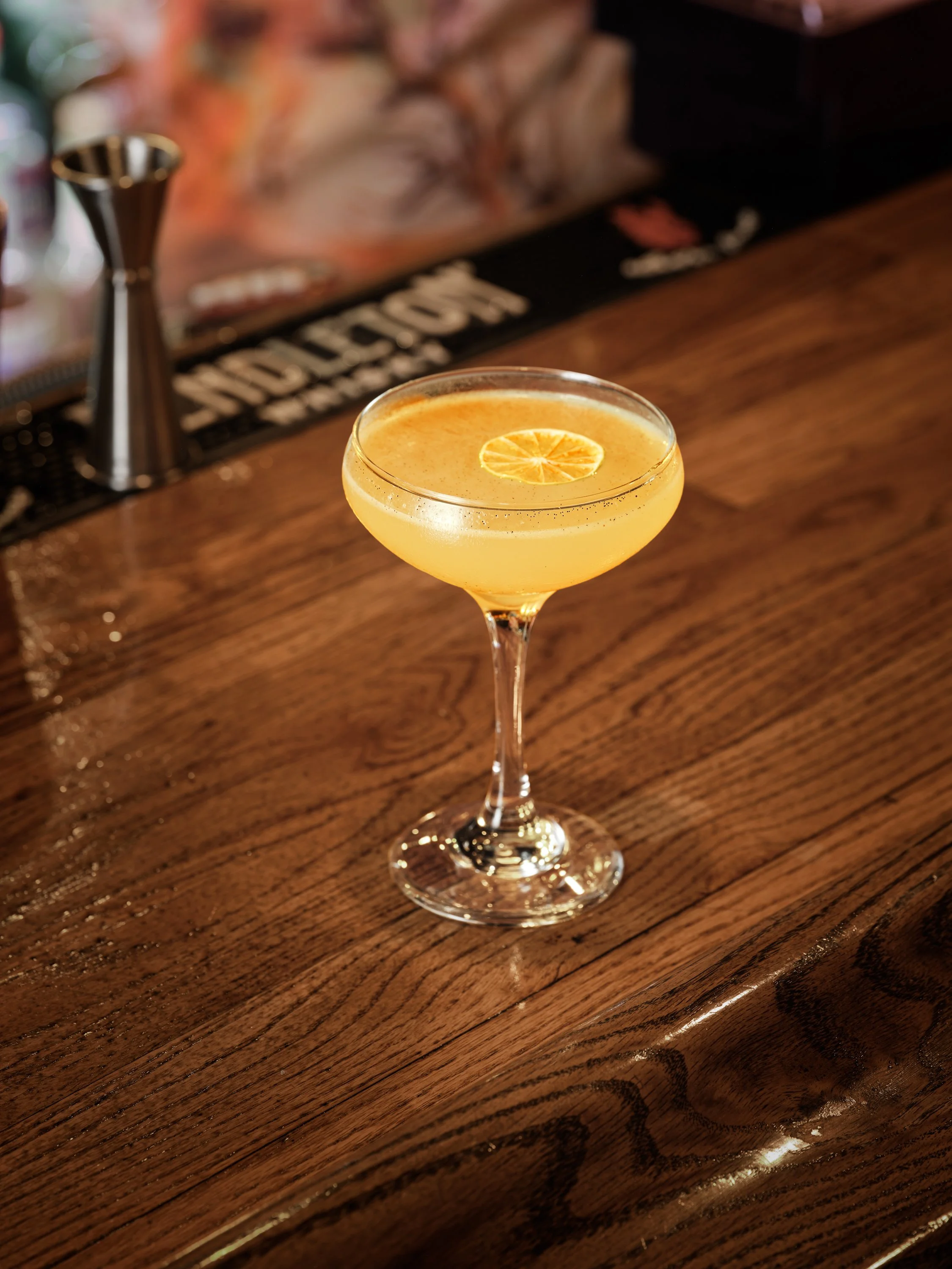 A cocktail with a lemon slice garnish on a wooden bar counter.