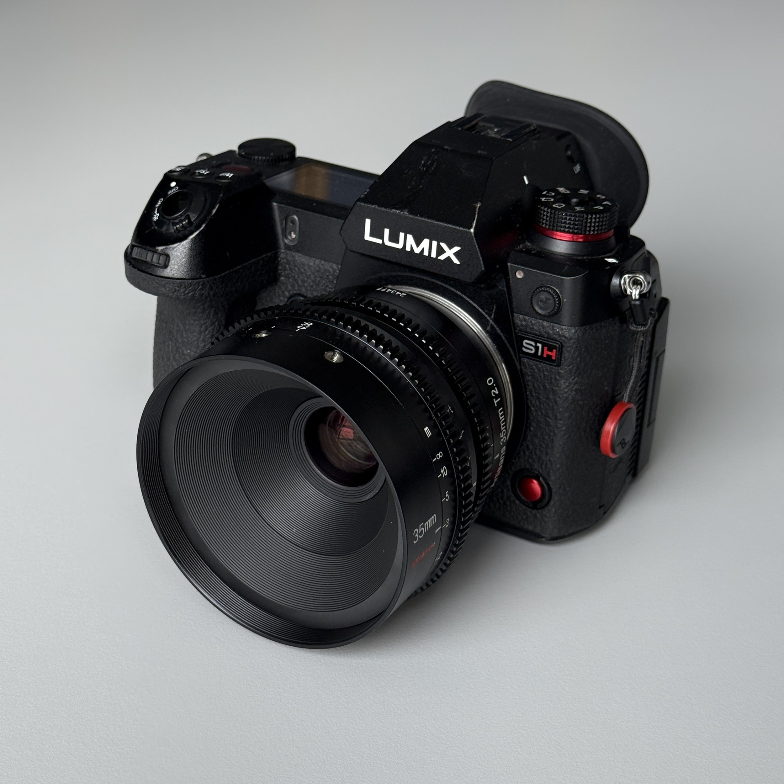 A black Panasonic Lumix S1H mirrorless camera with a 35mm lens attached, placed on a light gray surface.