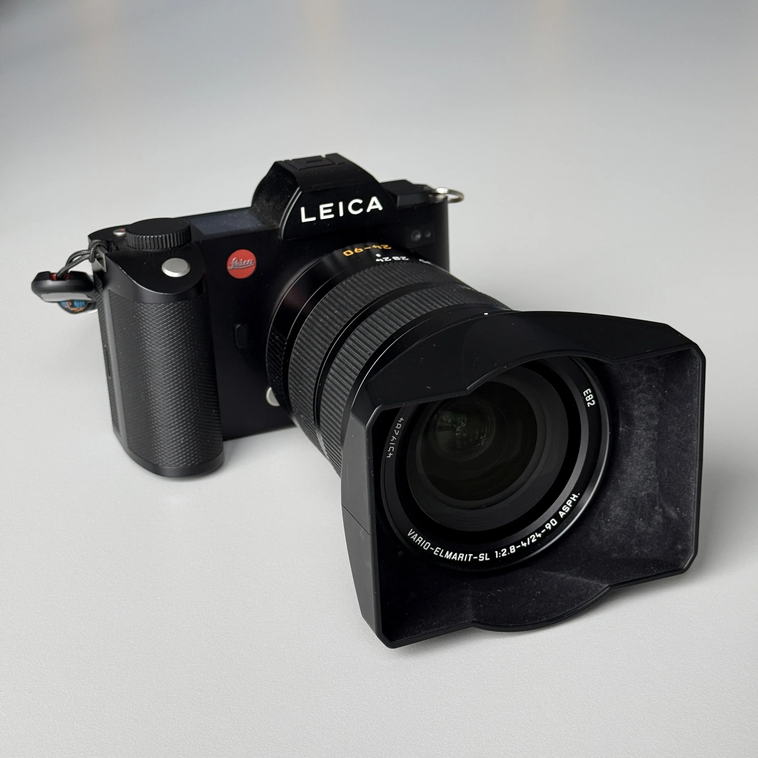 A black Leica camera with a large lens and lens hood on a light gray surface.