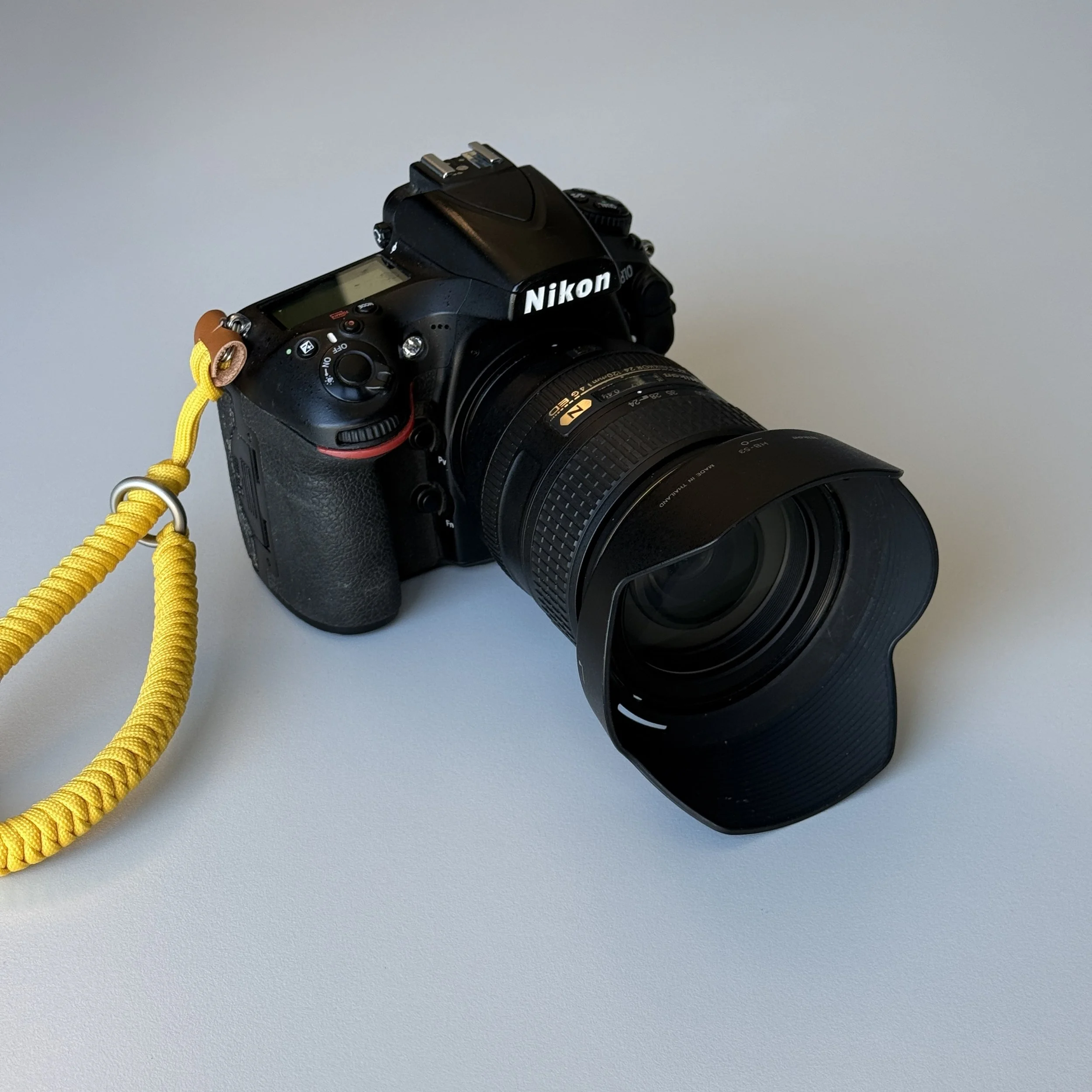 A black Nikon DSLR camera with a zoom lens and a yellow wrist strap on a light gray surface