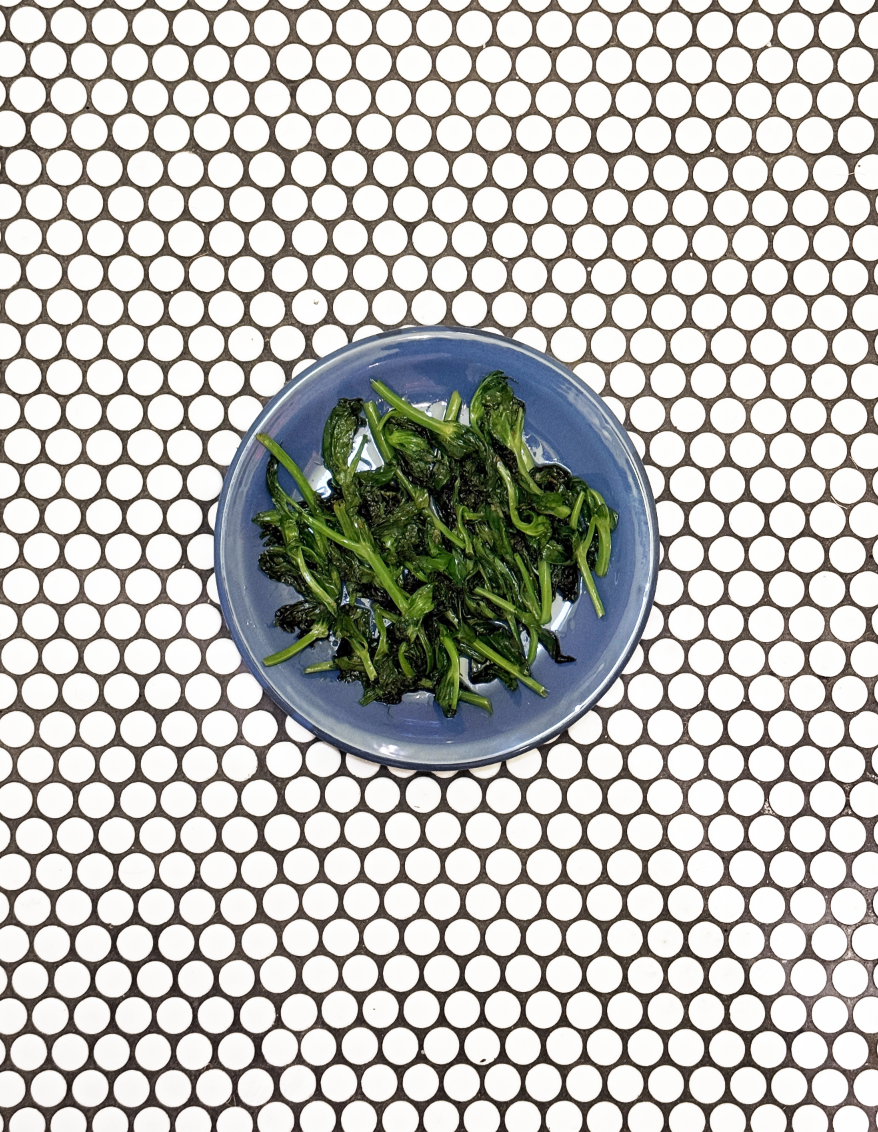 A blue plate with sautéed greens on a white and black polka dot table.