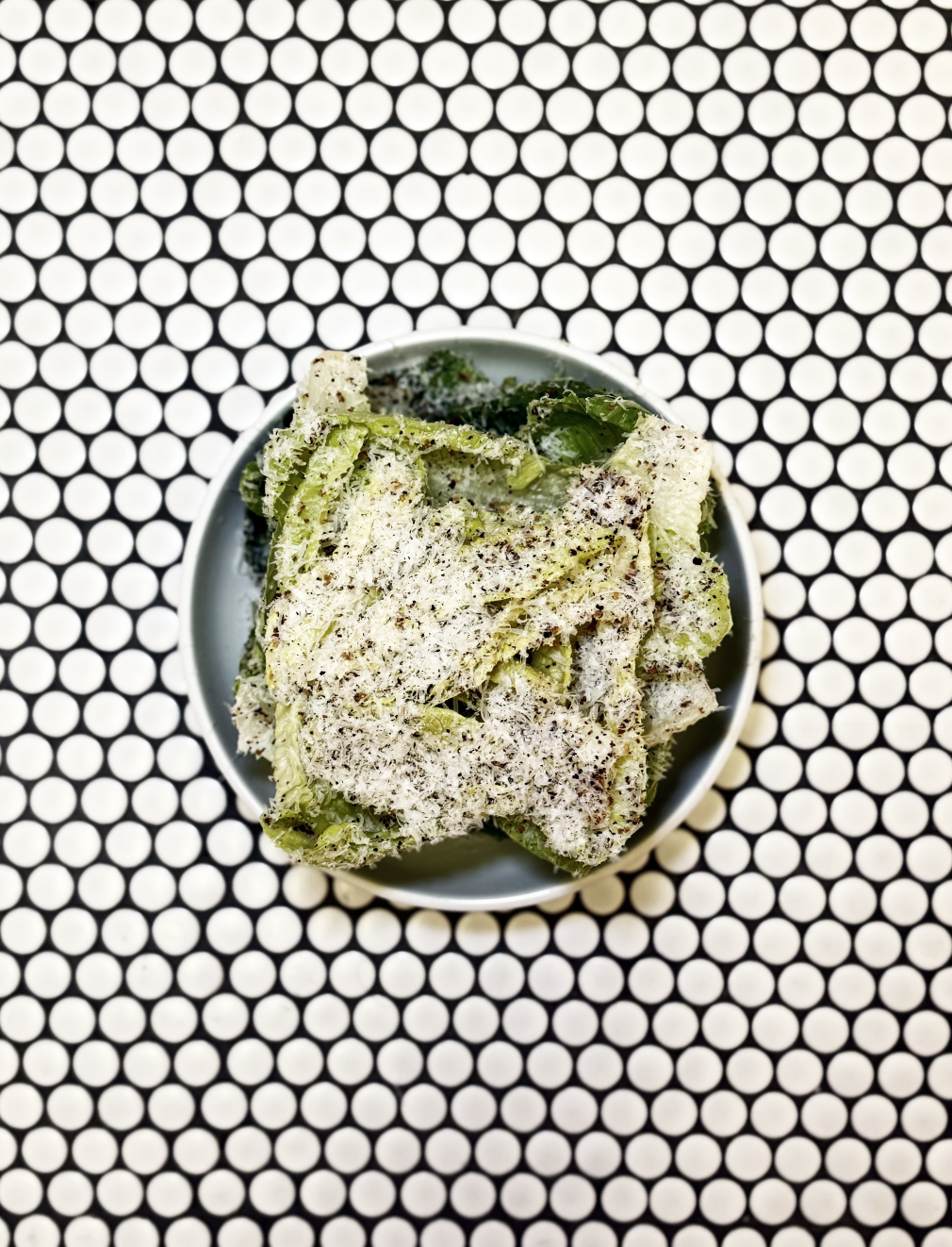 Bowl of Caesar salad with grated cheese and pepper on geometric background.