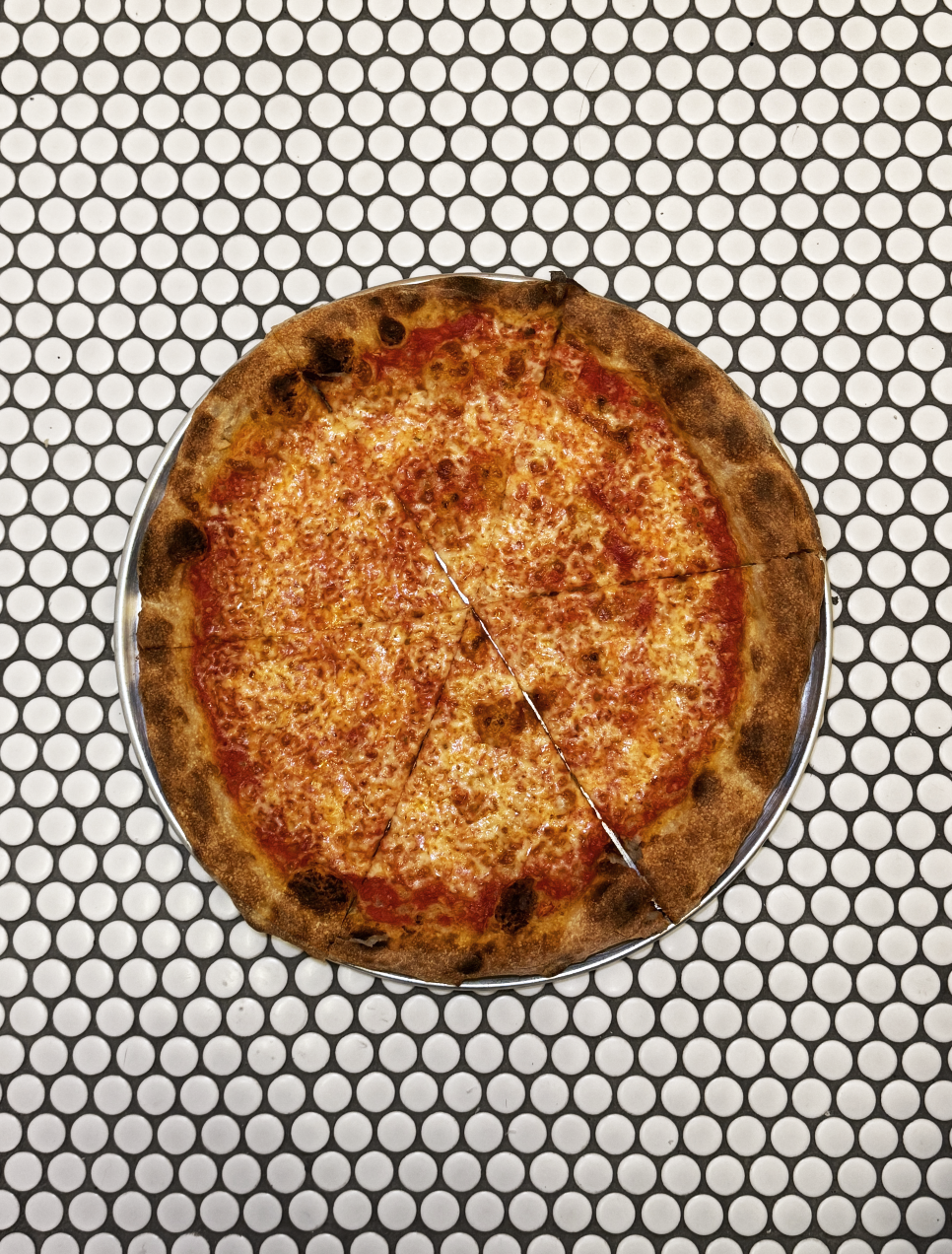 A cheese pizza with tomato sauce on a white circular tile table.