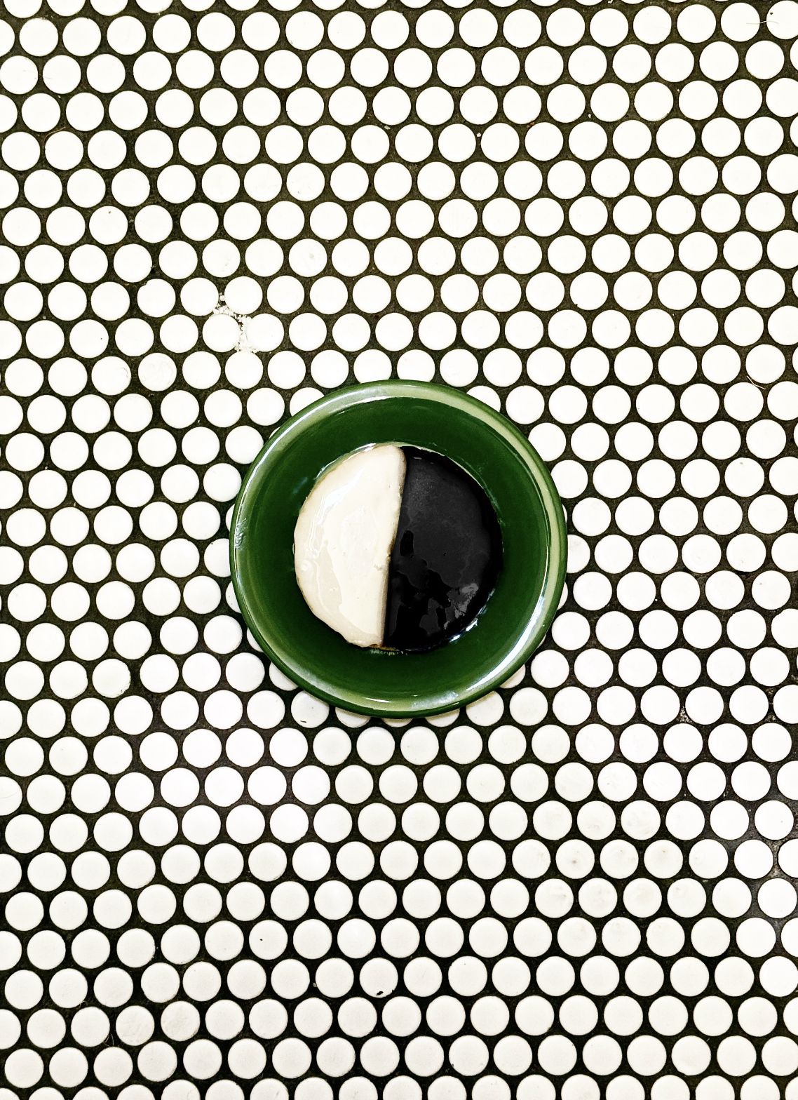 A black and white cookie on a green plate on a circular tile patterned surface.