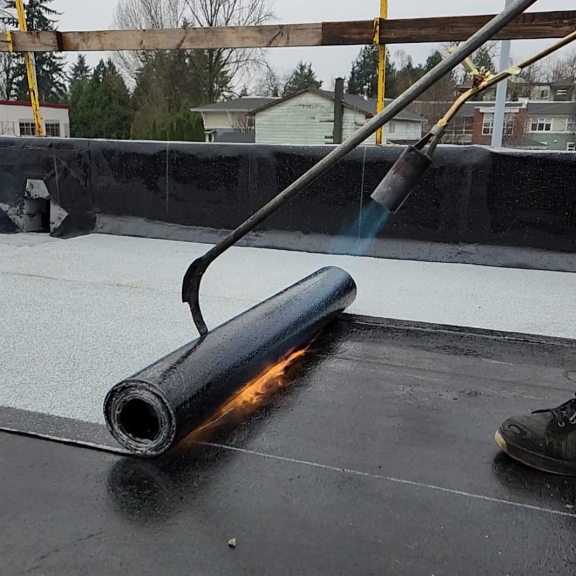 A person using a blowtorch to apply roofing asphalt on a roof surface during construction.