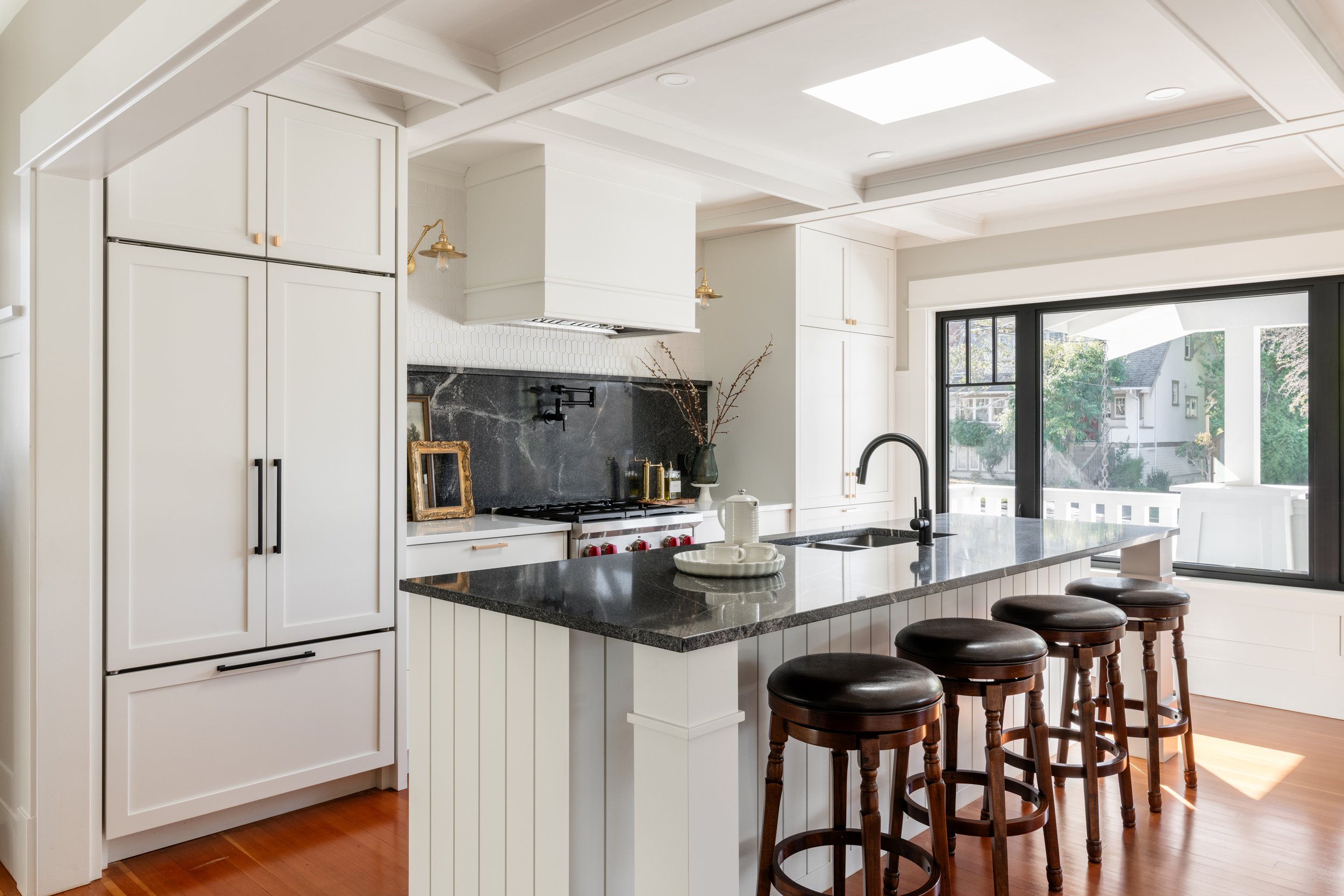 Modern kitchen with white cabinets, black granite countertops, a large window, and a kitchen island with seating.