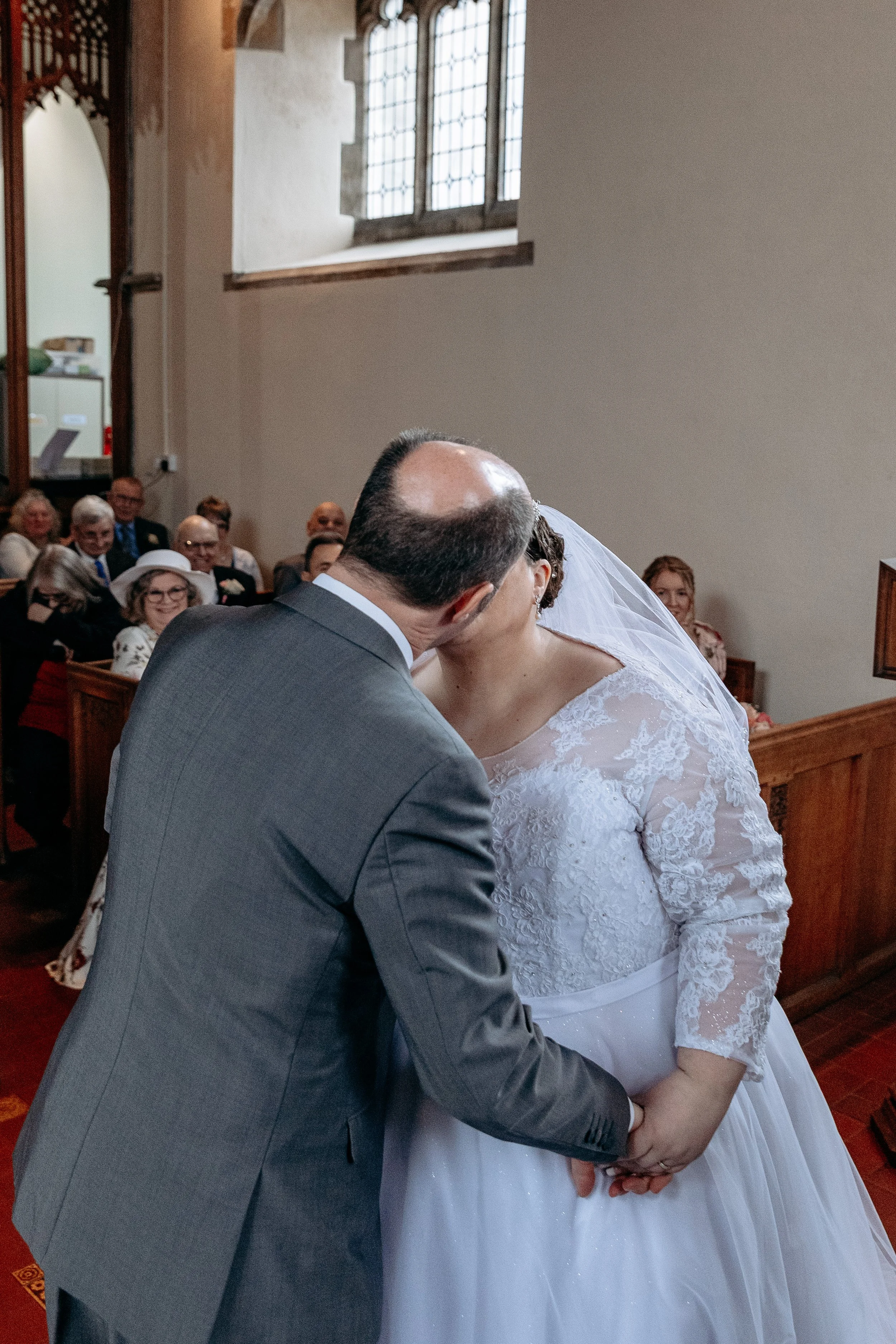 Bride and groom sharing a kiss during their wedding ceremony in a church, with guests seated in the background.