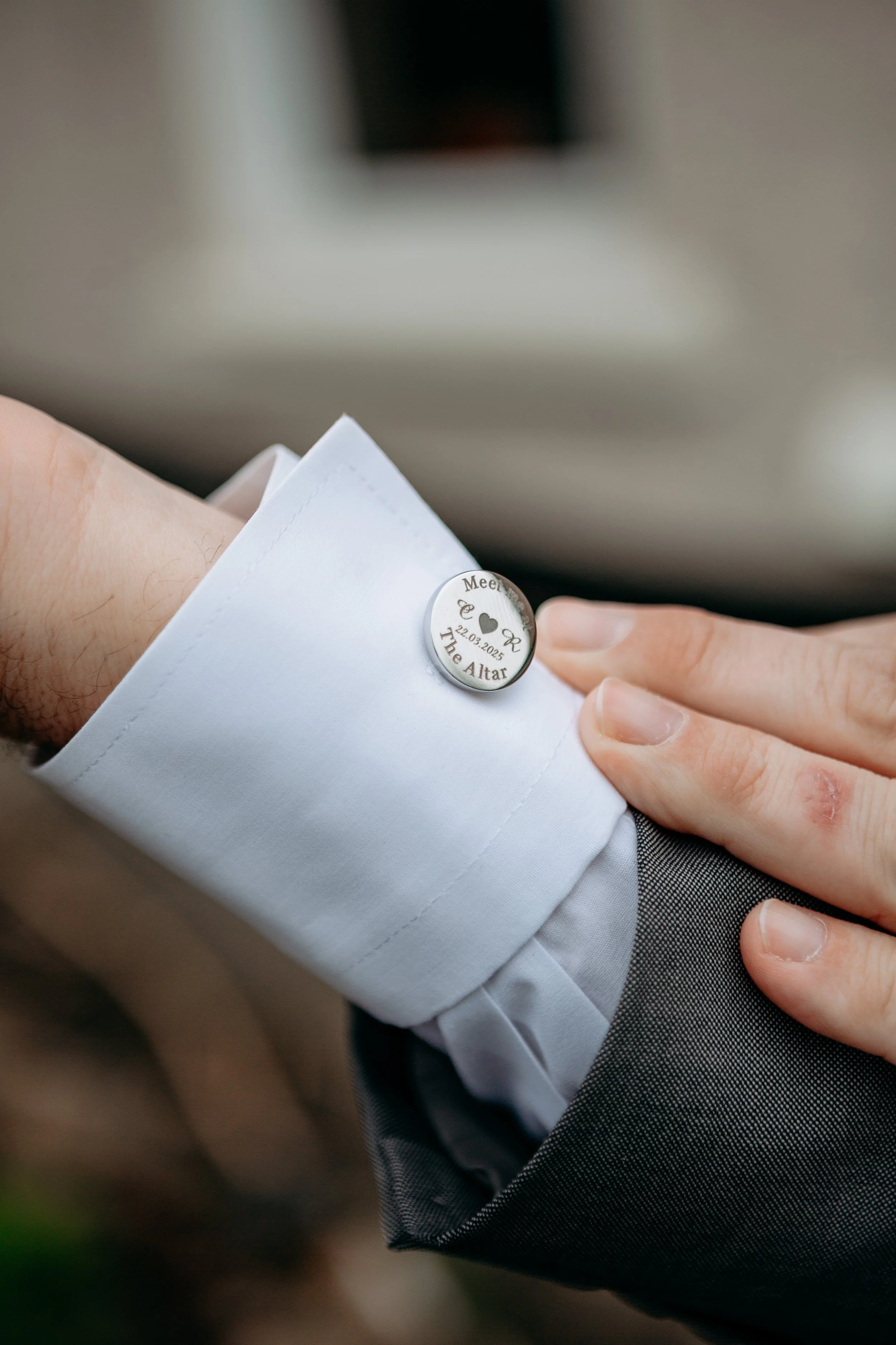 Close-up of a wedding ring worn on a person's finger, with the person dressed in a white shirt and gray suit, indicating a wedding ceremony or event.