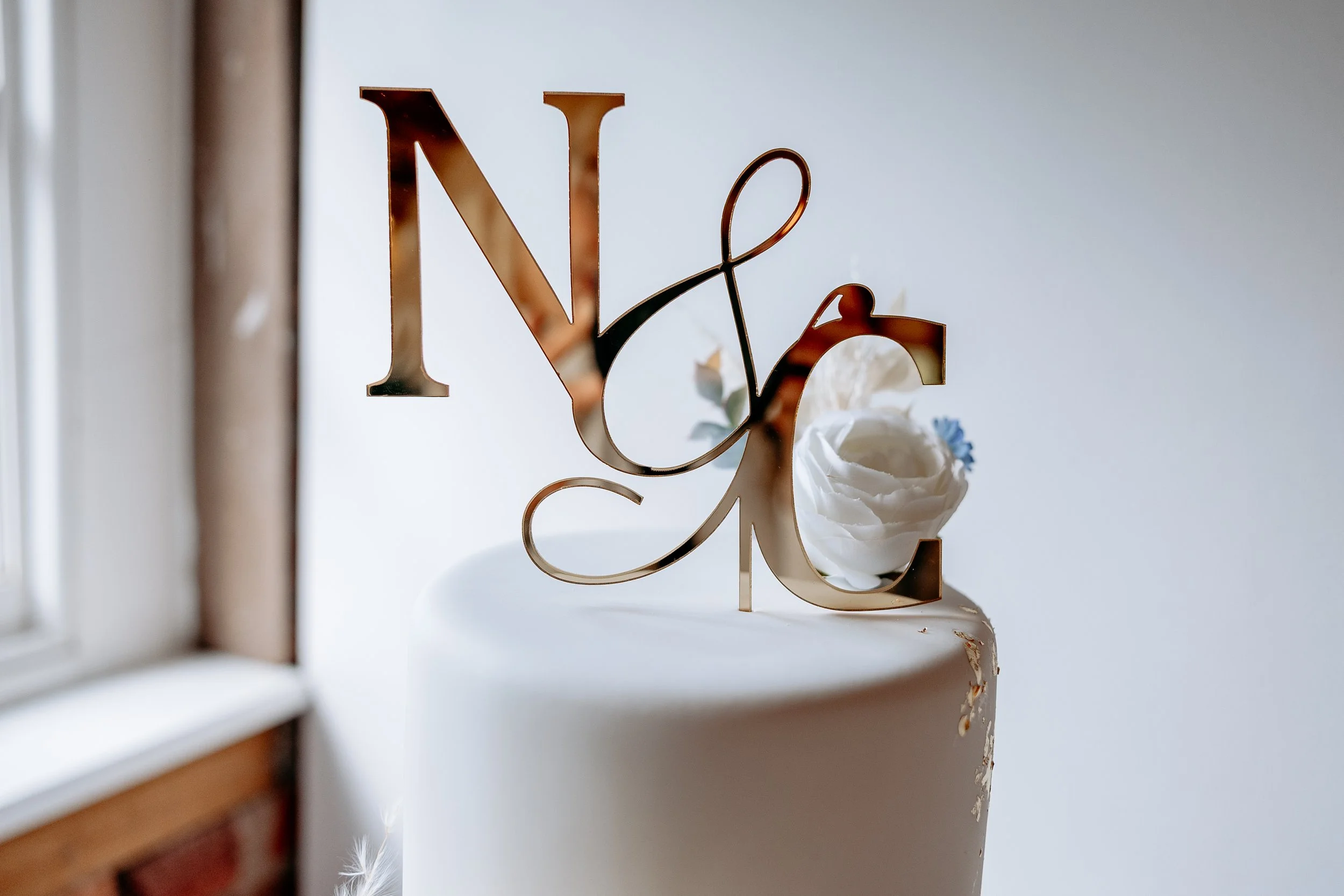 A cake topper with the words 'Love' in gold letters, decorated with white and blue flowers on a white cake.