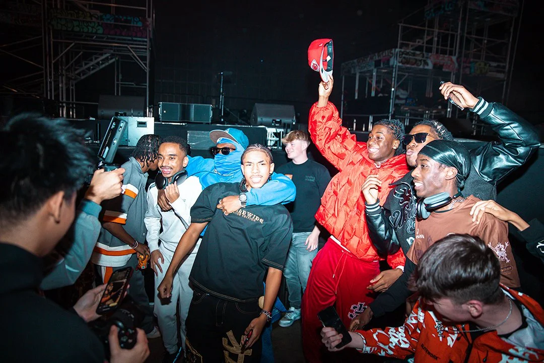 Group of young people dancing and taking photos at a concert or party, with stage equipment in the background.