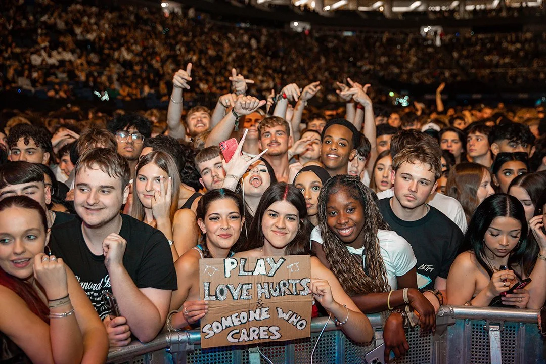 Crowd at a concert holding a sign that says "Play Love Hurts & Someone Who Cares."