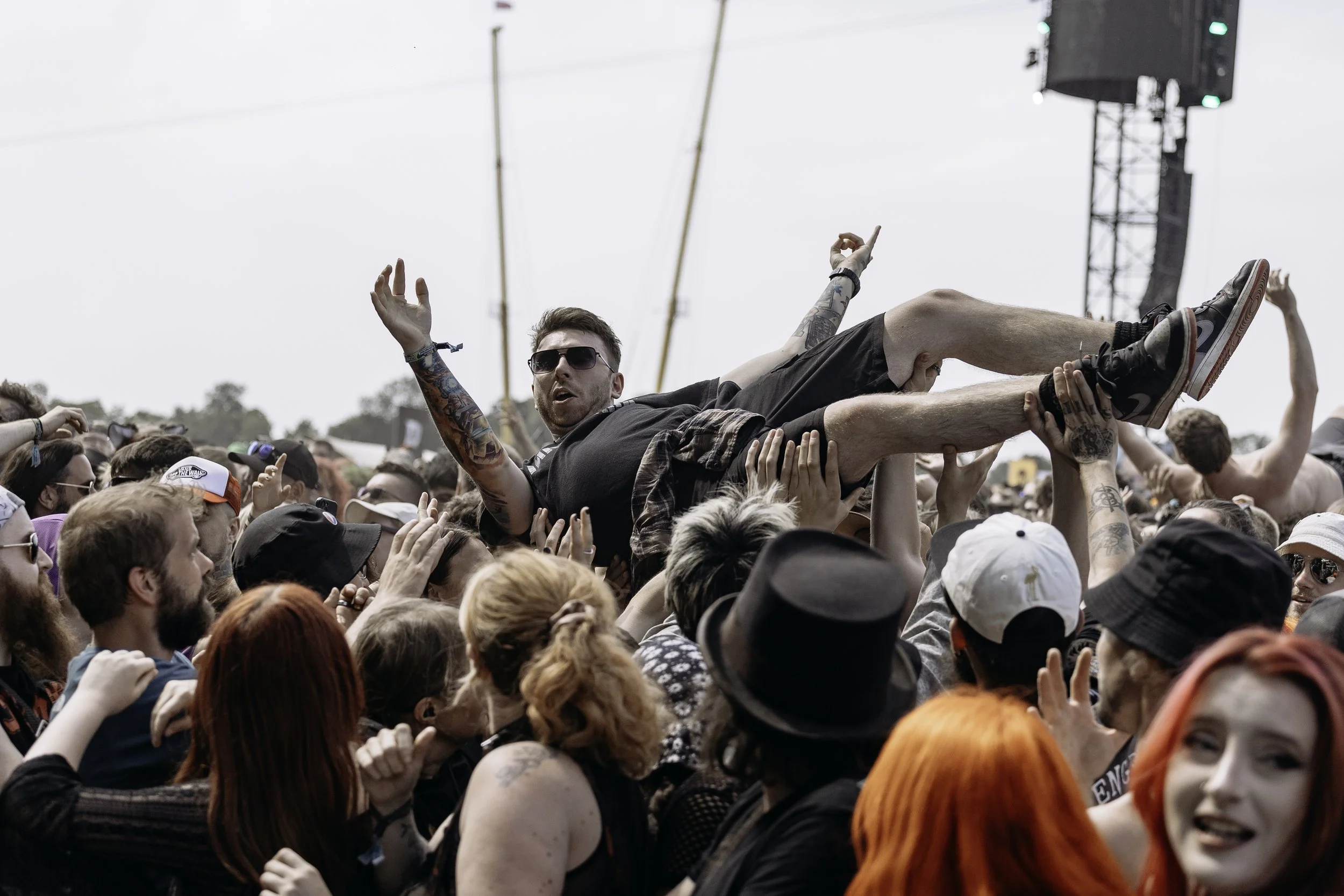 Crowd at a concert or festival with a man in sunglasses crowd surfing above others.