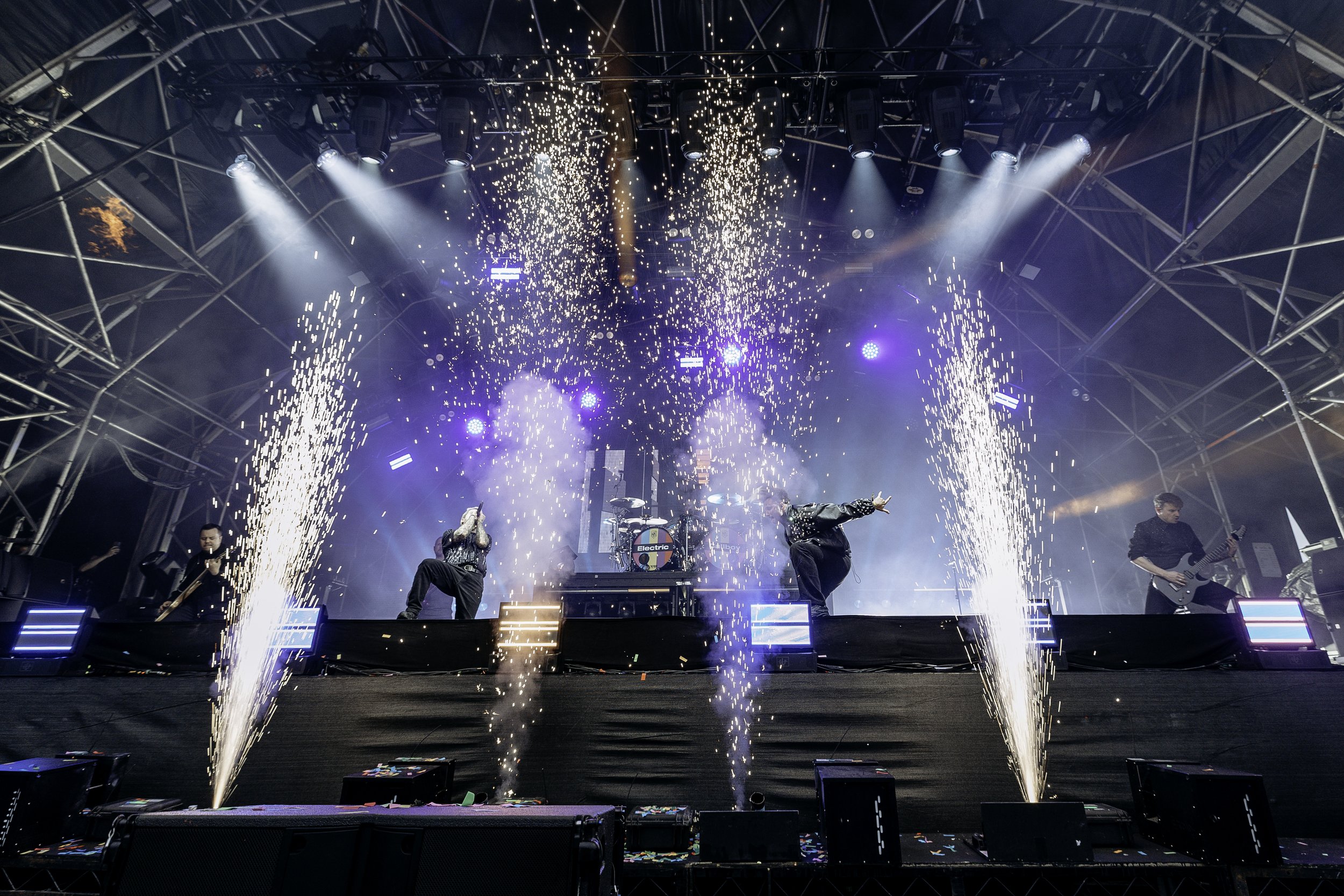 A live music concert with performers on stage, pyrotechnics, and bright stage lights