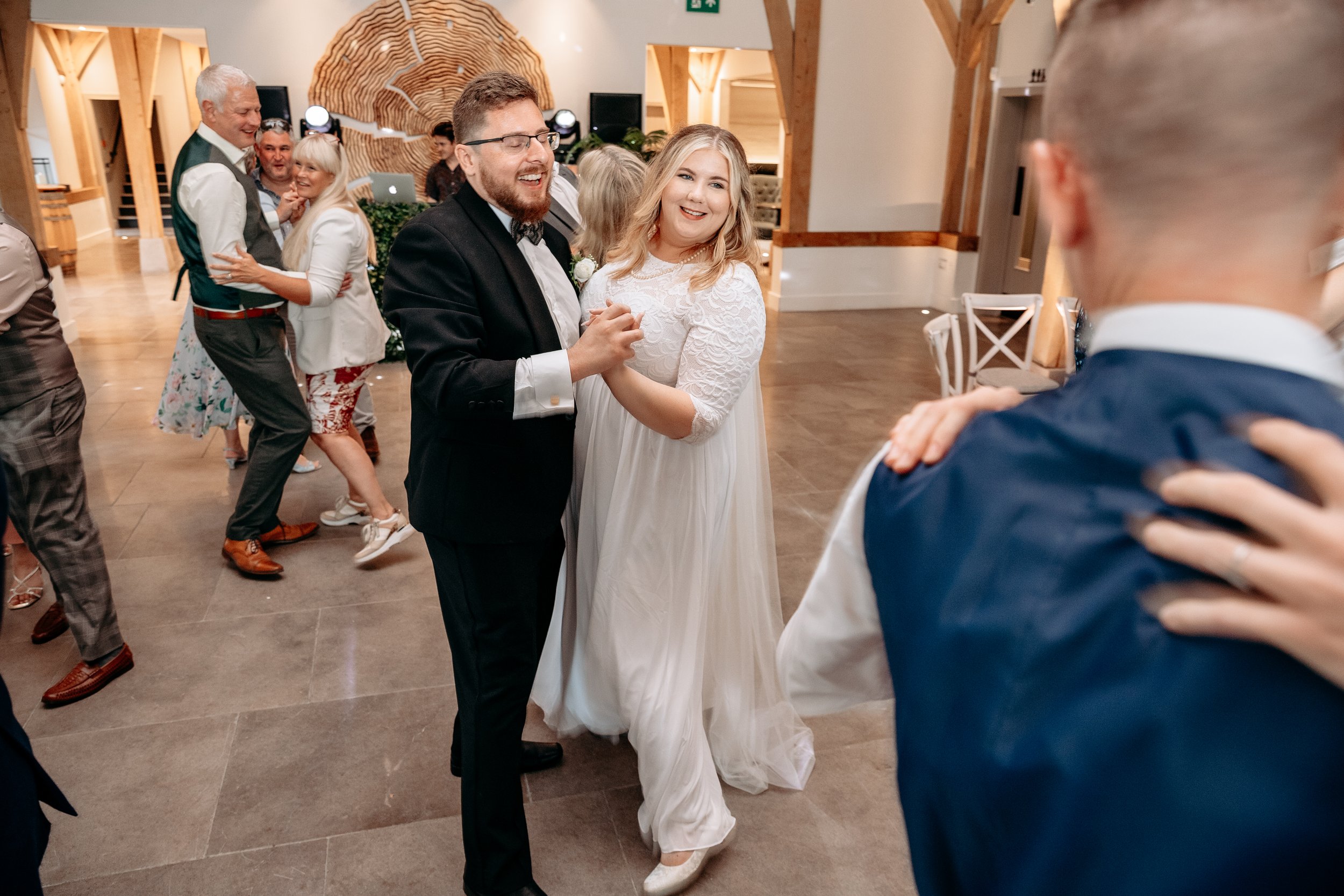 Couple dancing at a wedding reception with other guests dancing in the background.