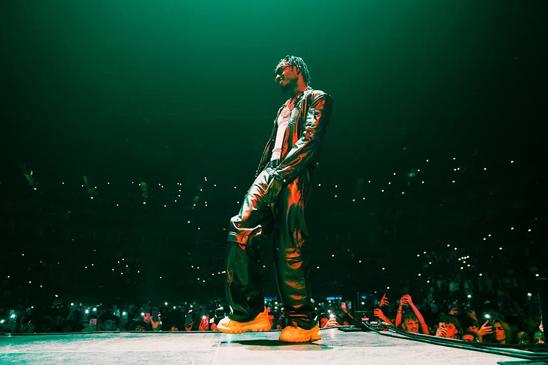 Performer in leather outfit on stage, surrounded by a crowd with glowing lights in a concert setting.