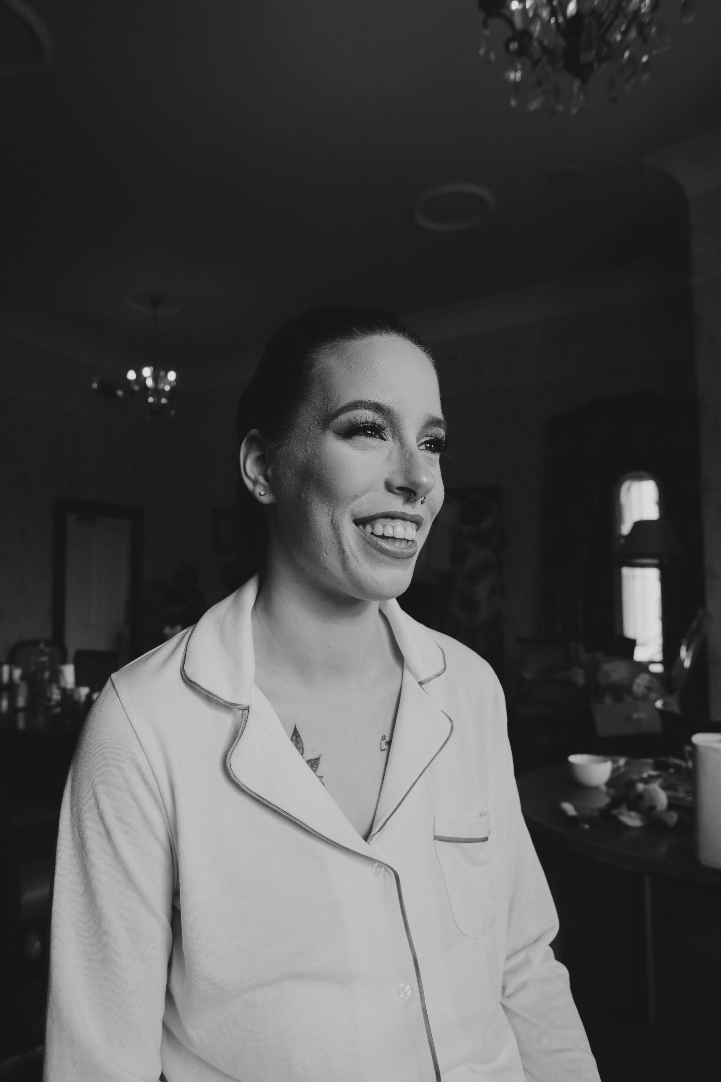 A woman with dark hair in a bun, wearing pajamas, smiling in a dimly lit room.