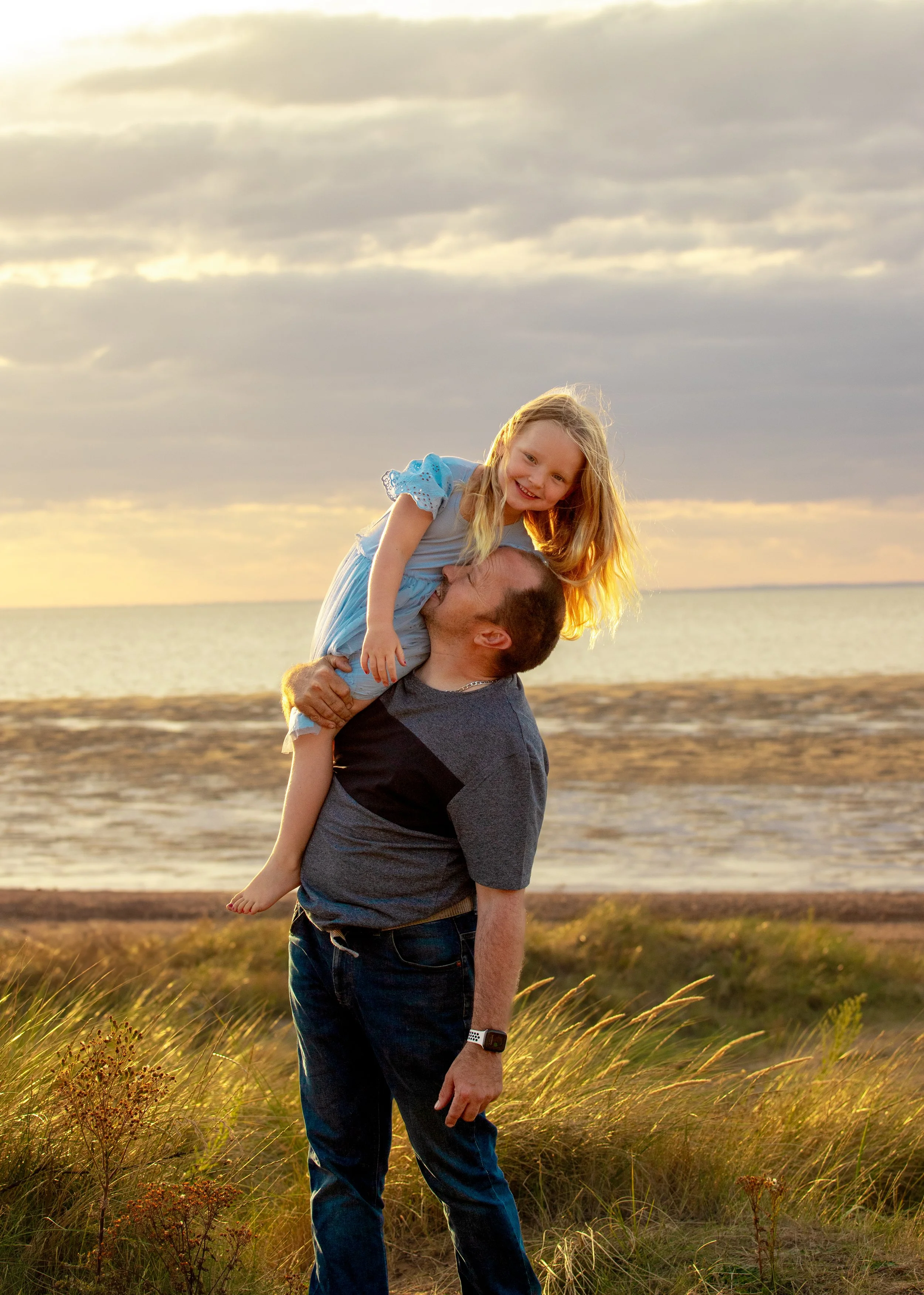 Man carrying a young girl on his shoulder near the beach at sunset.