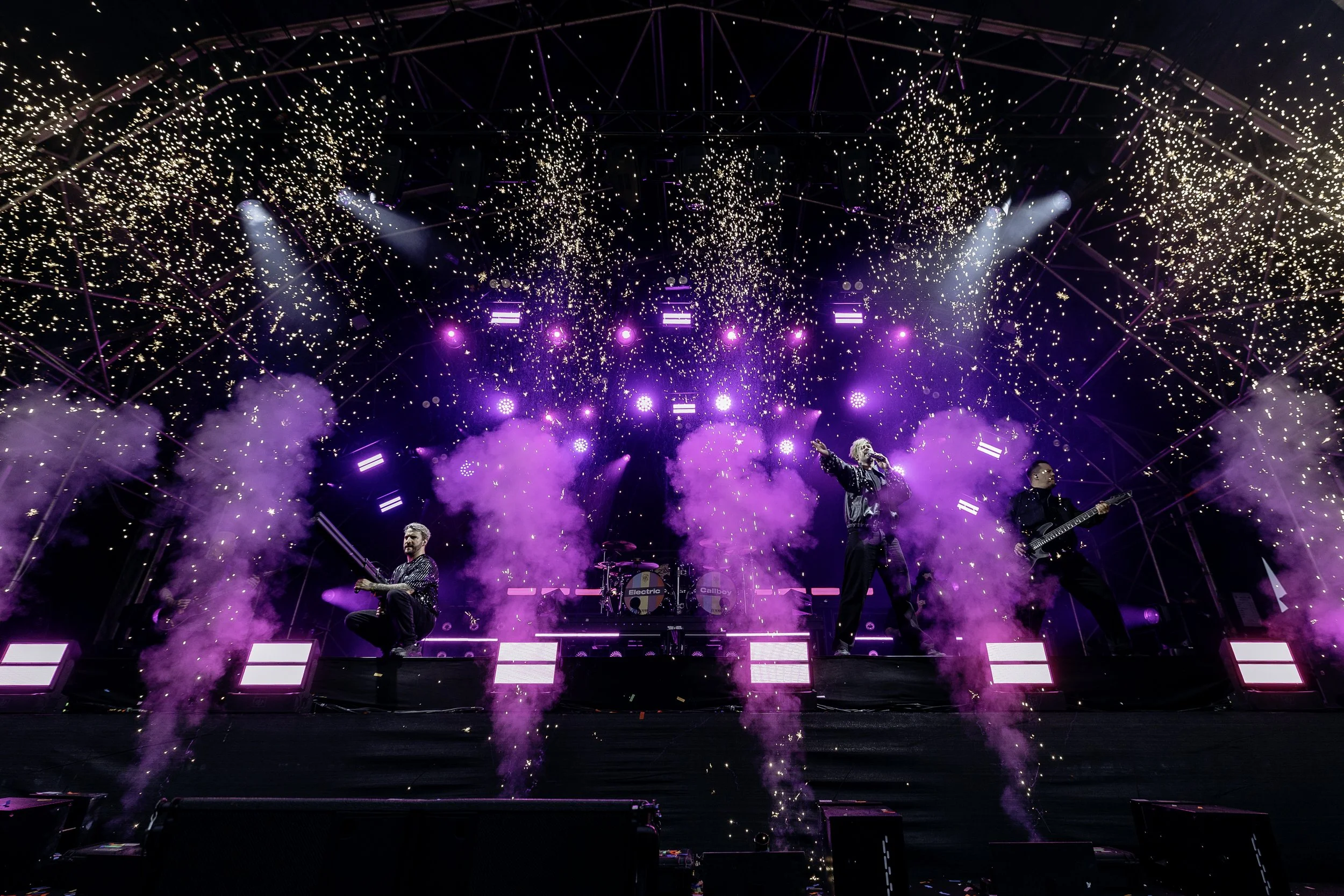 Music band performing on stage with purple lighting, smoke, and fireworks.