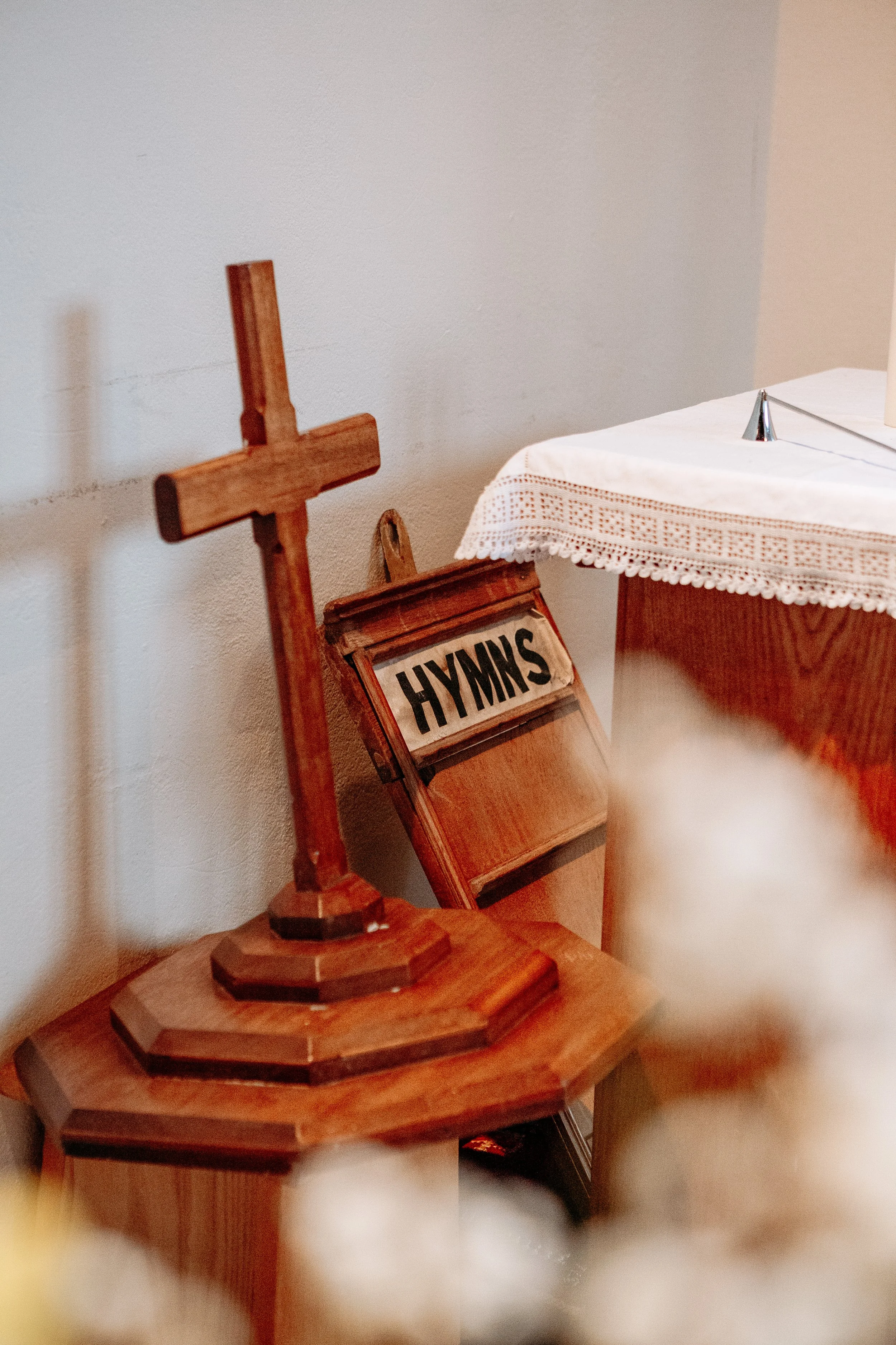 A wooden cross, a hymn book, and a table with a lace tablecloth inside a church.
