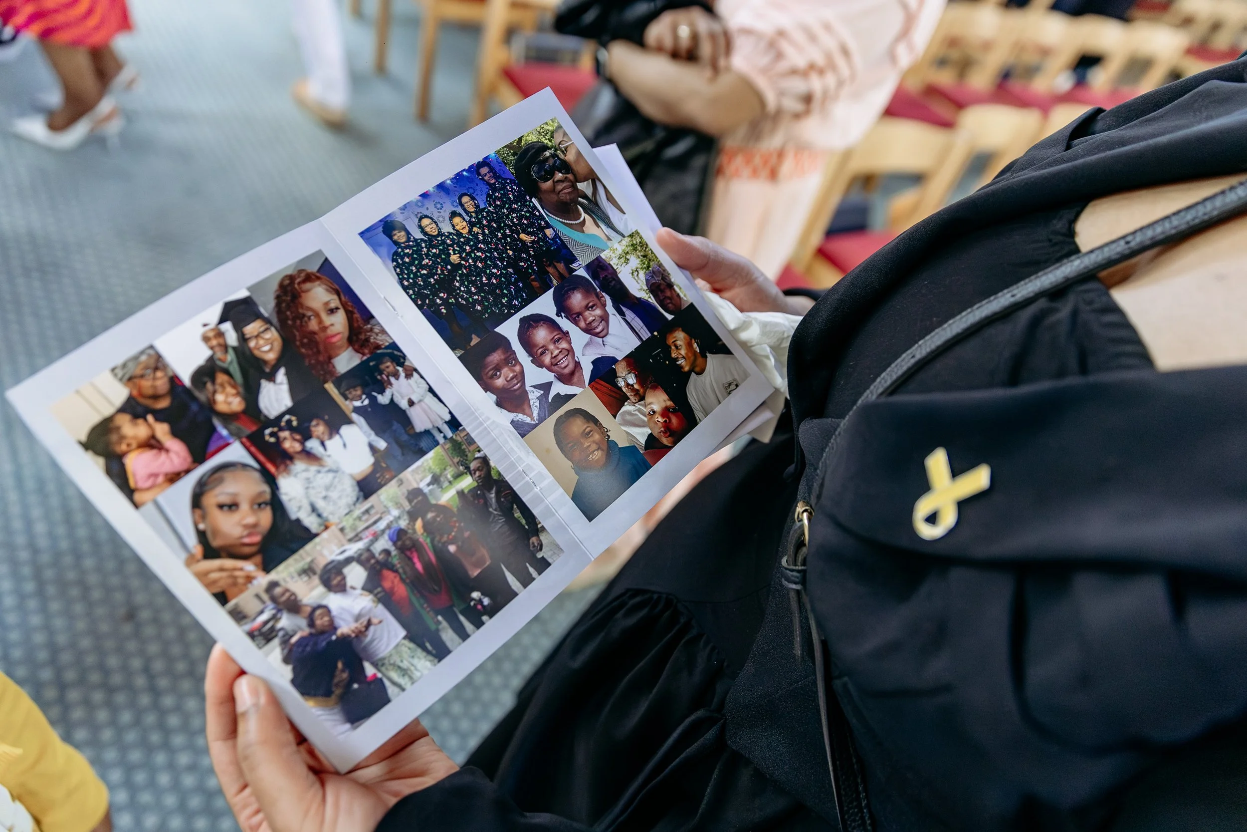 A person sitting in a venue looking at a photo collage of various people and groups, including children and adults, with others seated in the background.