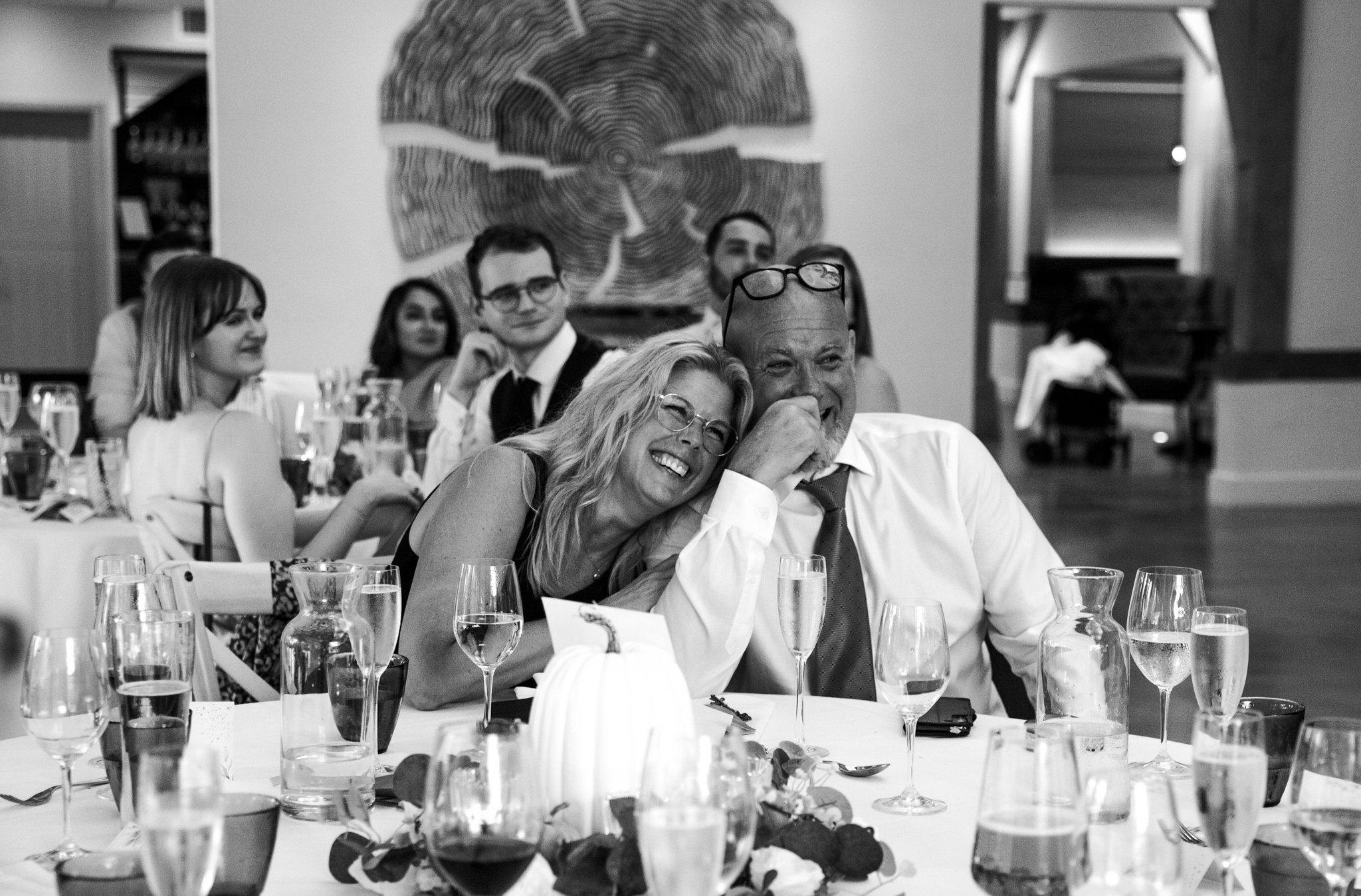 Guests at a wedding reception sitting at a table with drinks and decorations, smiling and enjoying the event.