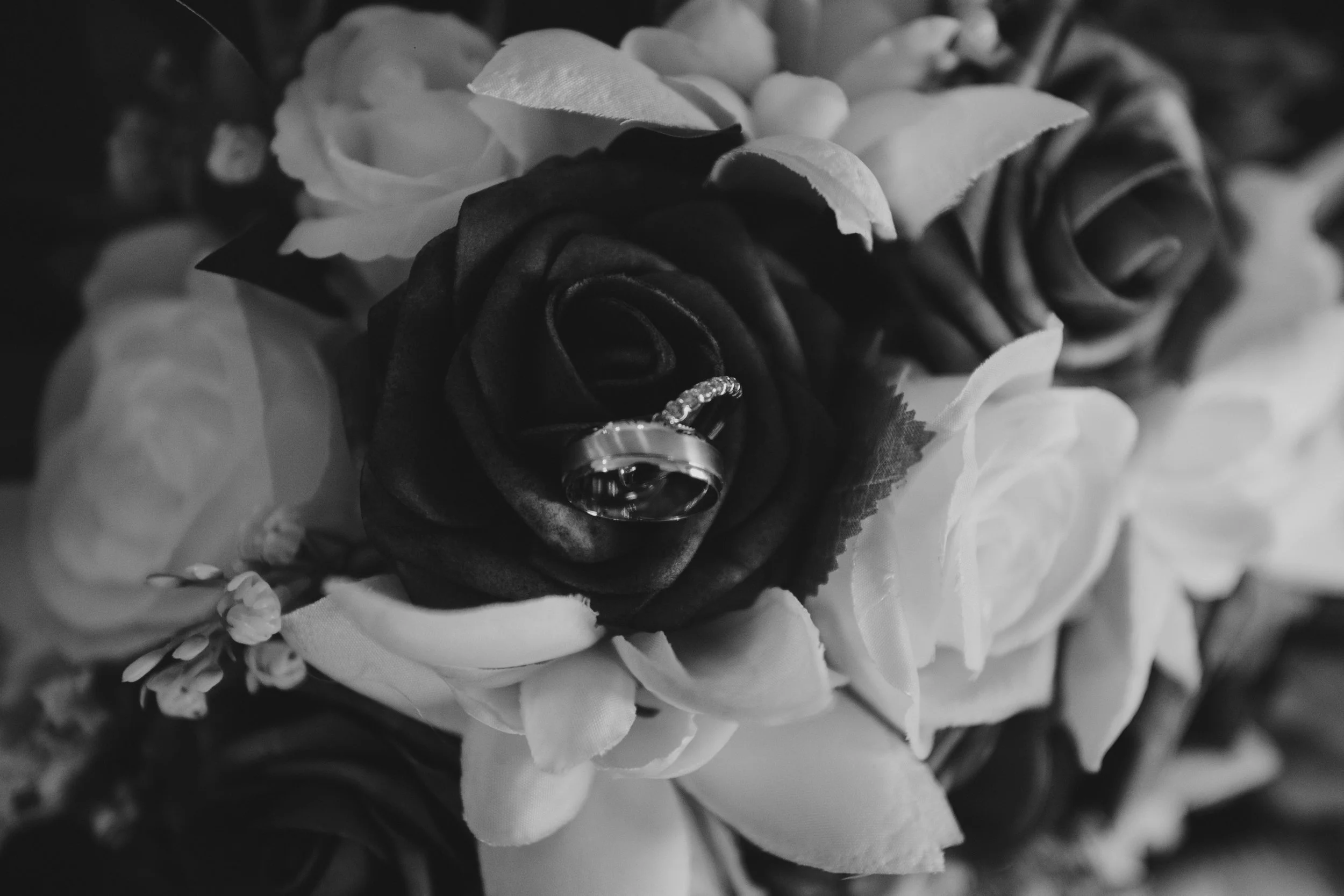 Black and white photo of a bouquet of flowers, with a wedding ring placed on a dark rose.
